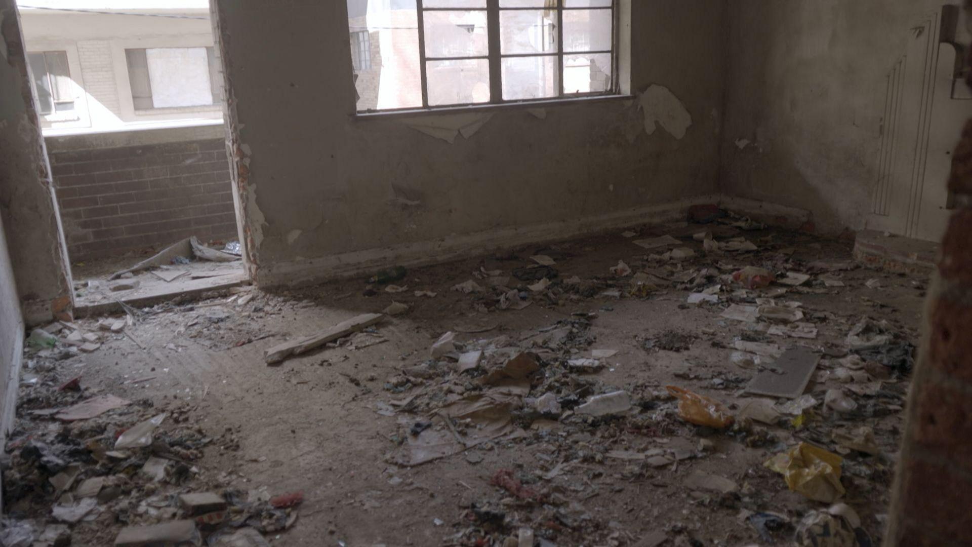 Litter and dirt are strewn across the floor of a derelict room at Vannin Court.