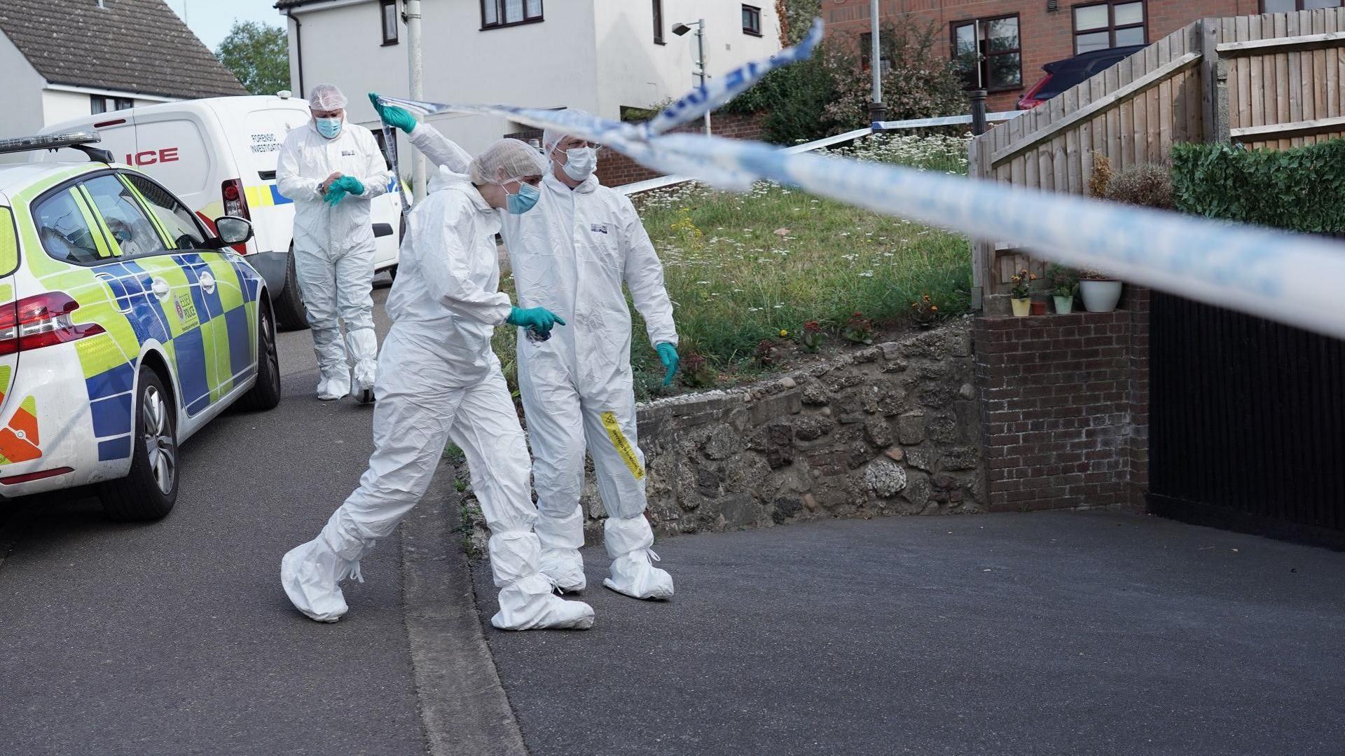 Forensic officers lifting police tape at the cordon, outside the property