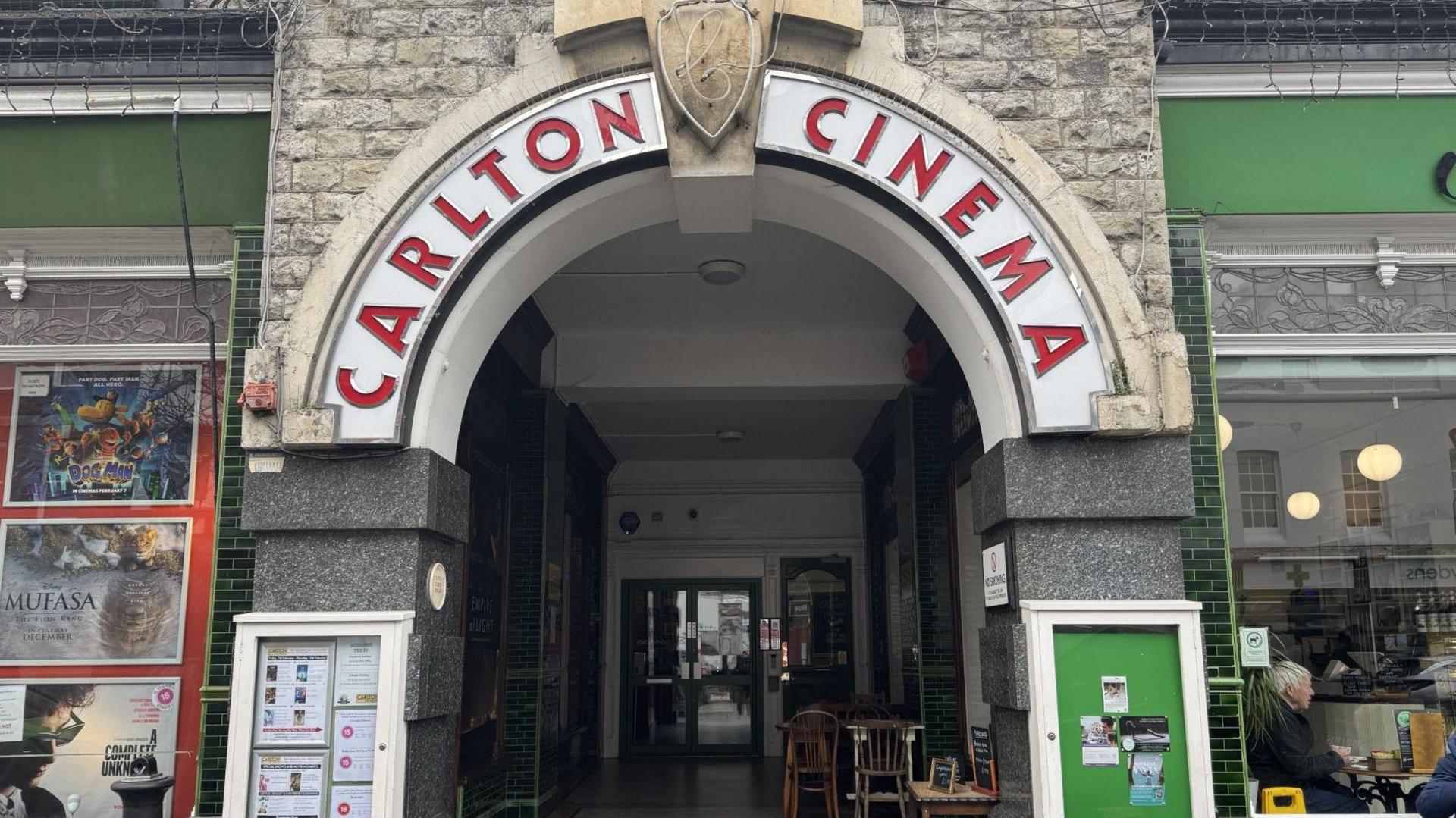 An exterior image of the Carlton Cinema in Westgate. 'Carlton Cinema' is spelt out over an arch and listings are available to the left. The panels of the building are painted green. 