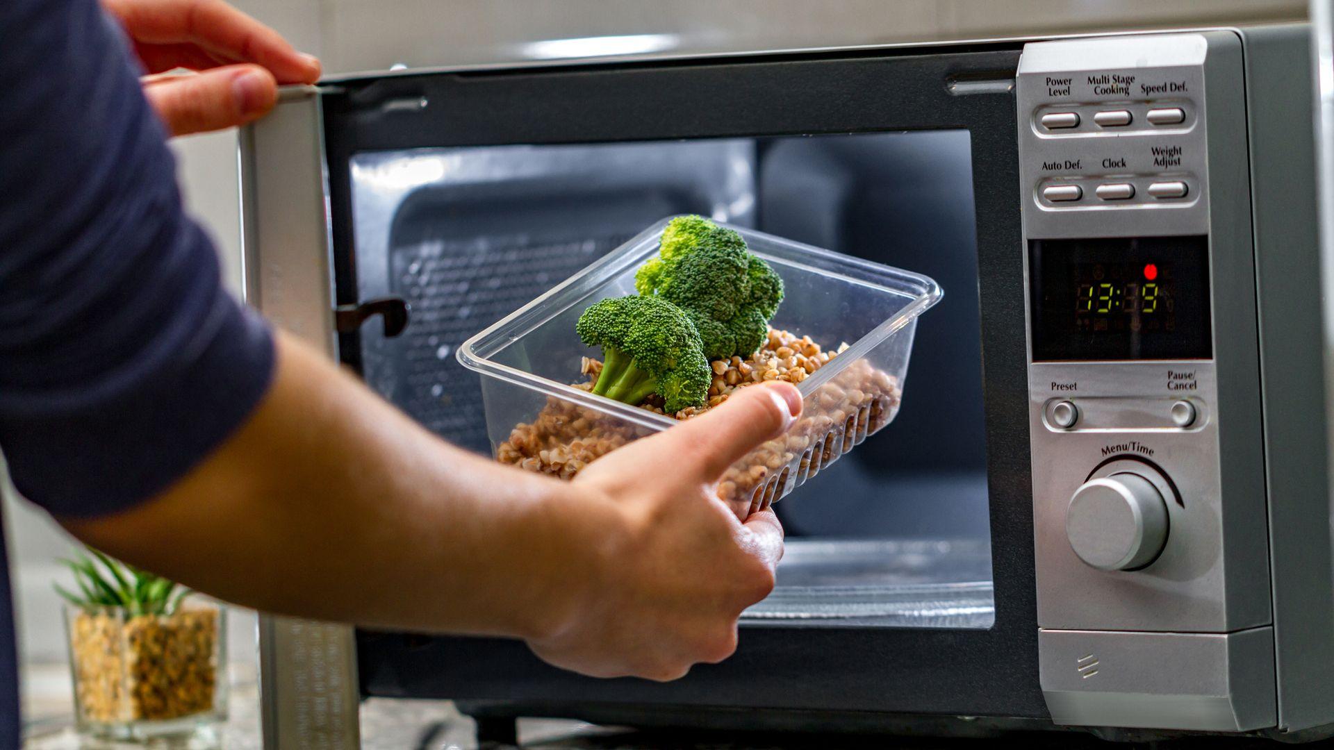 Man puts plastic container containing food in a microwave.