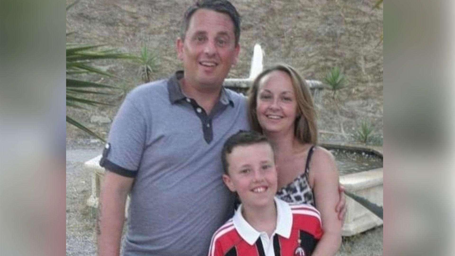 Dyn mewn crys-t glas gyda'i fraich o amgylch ei wraig. Mae plentyn mewn crys chwaraeon coch a du yn sefyll o'u blaenau.