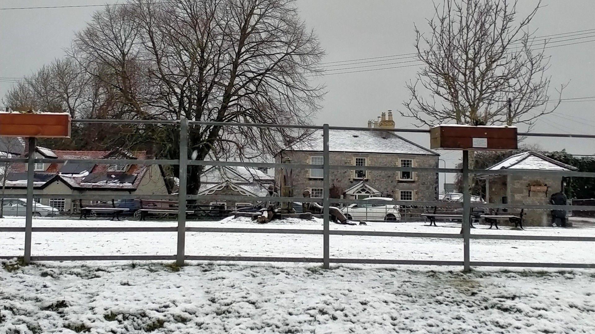 row of houses with snow on the rooves and on the grass and fence in the foreground with a grey sky overhead
