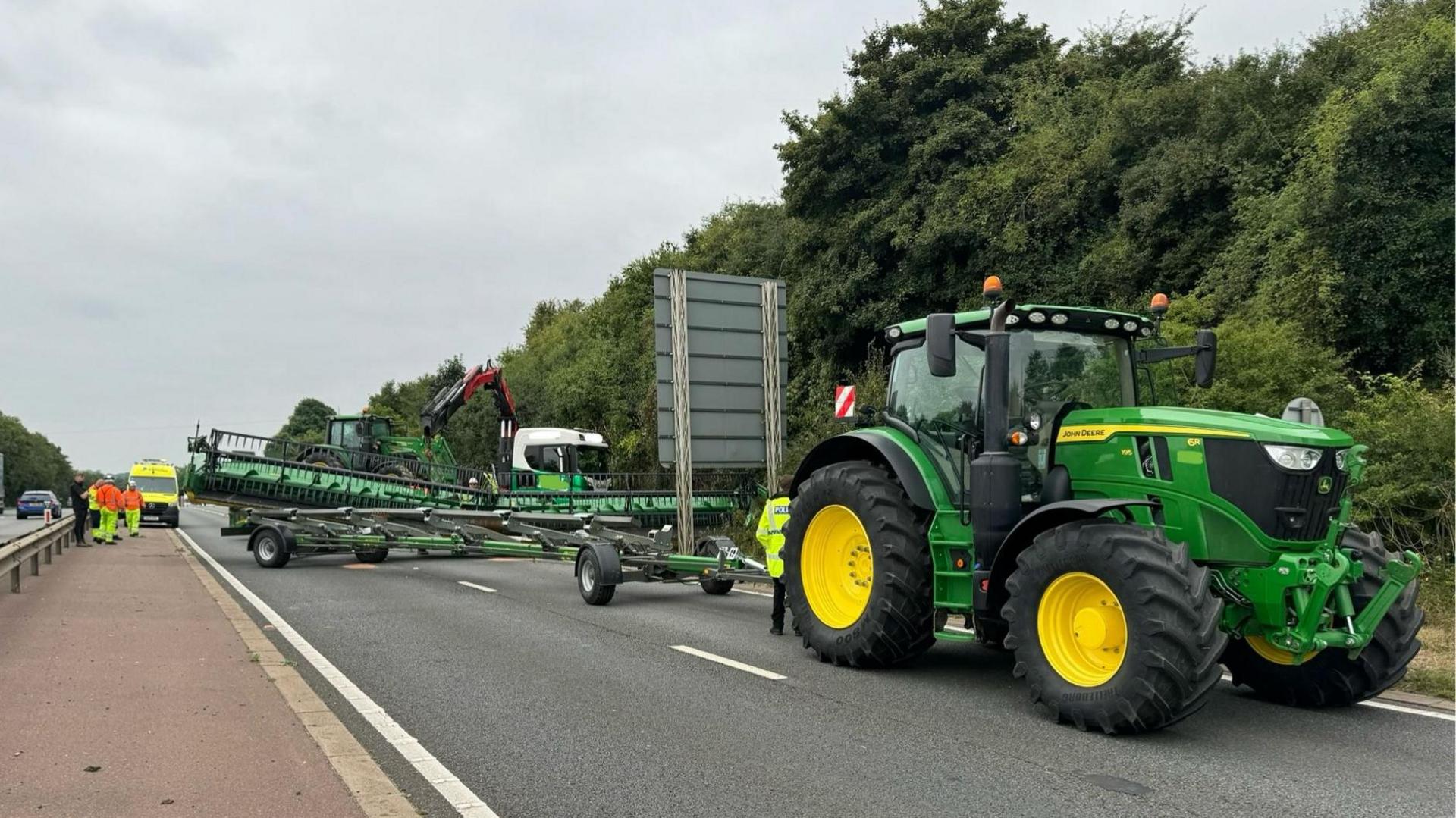 A combine harvester off the back of a green tractor, it can be seen covering a road.