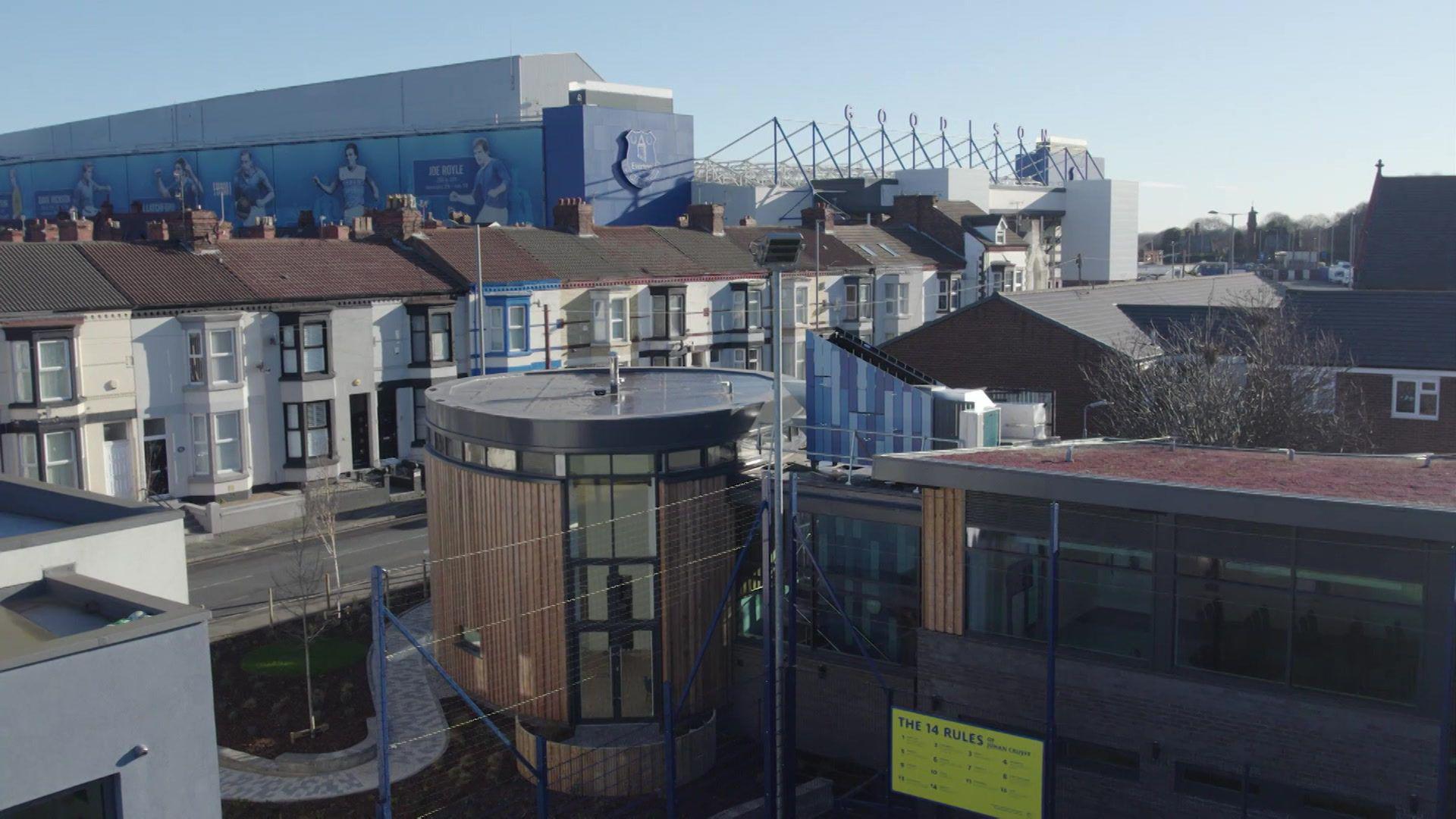 An aerial view of Goodison Park stadium, with a row of terraced houses and office buildings in the foreground