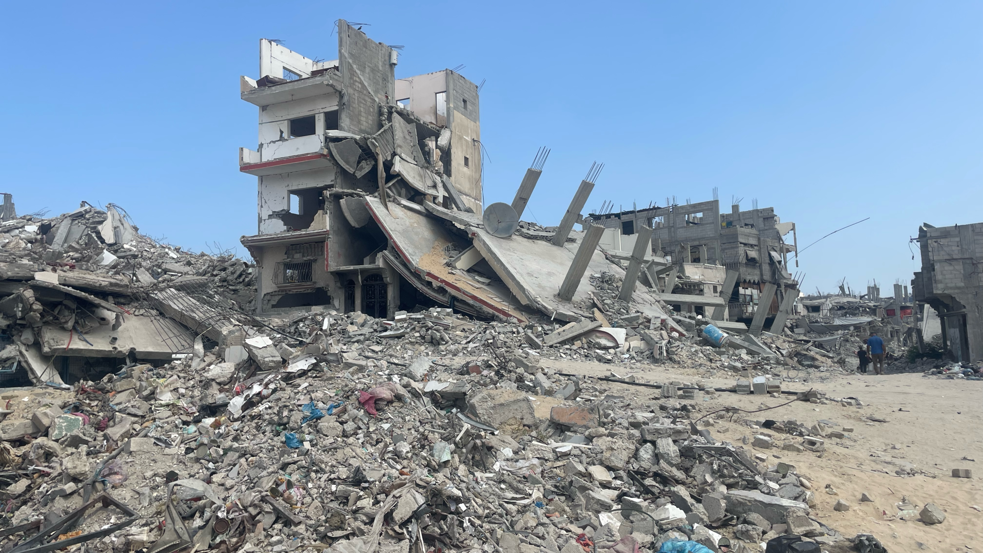 Rubble from destroyed buildings is heaped up beside structures that are still standing but uninhabitable. In the foreground, a wrecked four-storey block has lost its roof and some walls.