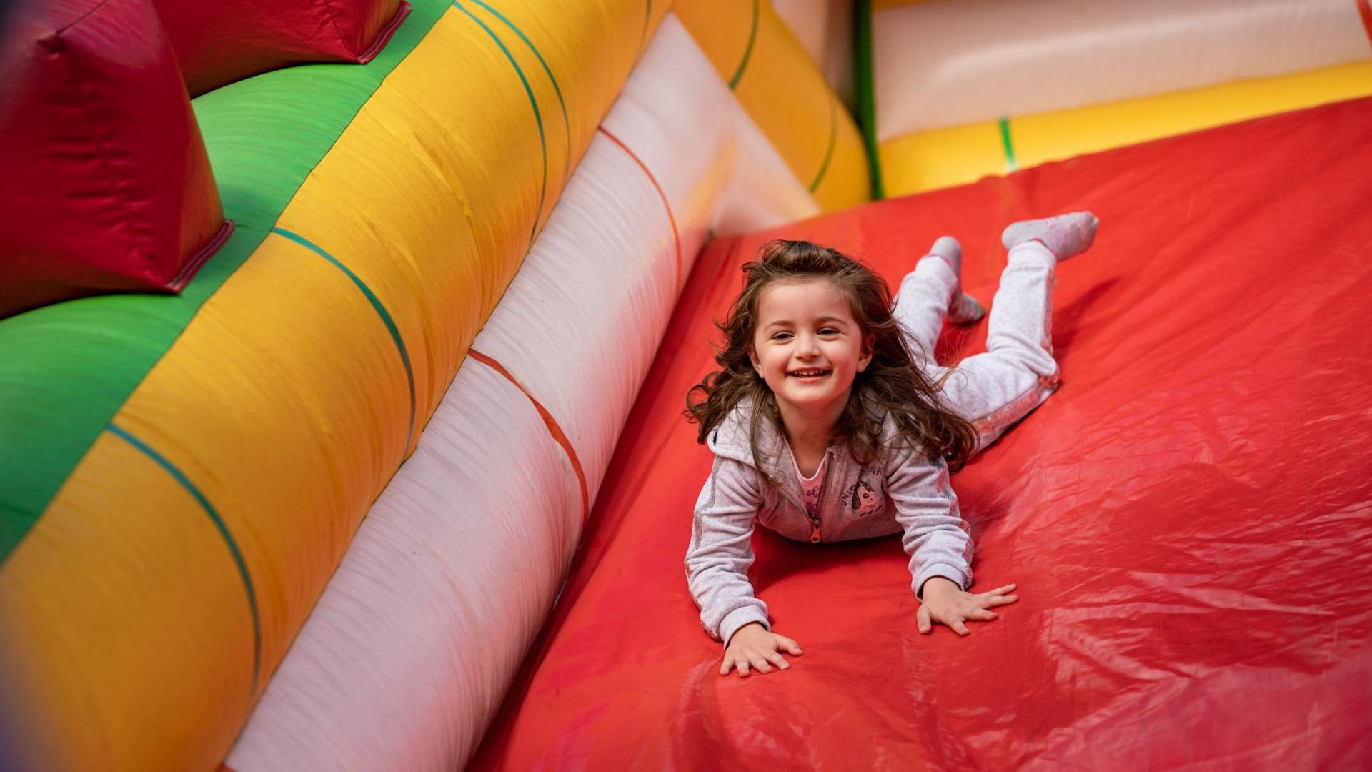 An image of a small girl playing on a red slide in an indoor inflatable play centre.