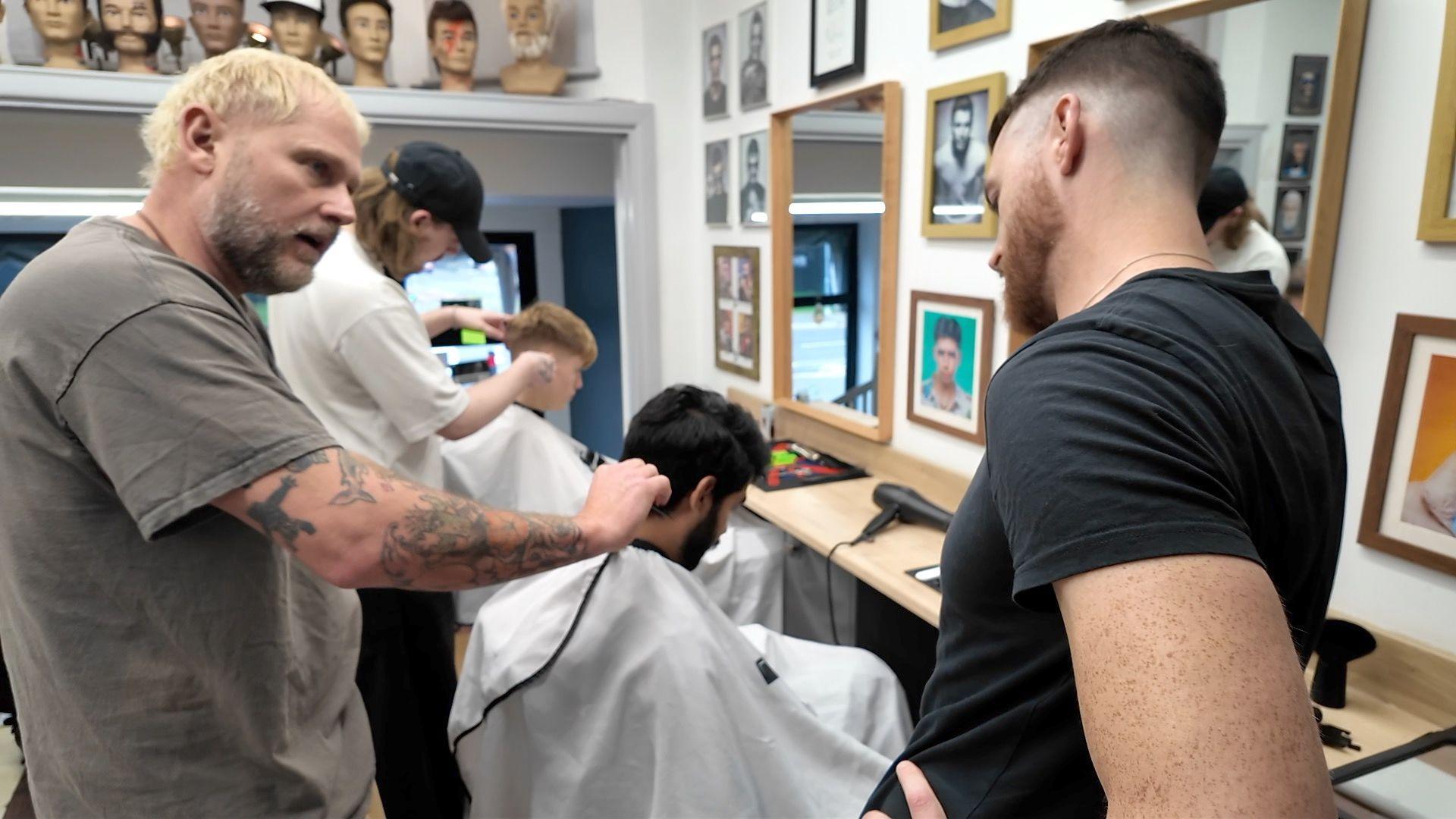 Mike Taylor left, talking to a student who is in the process of cutting someones hair