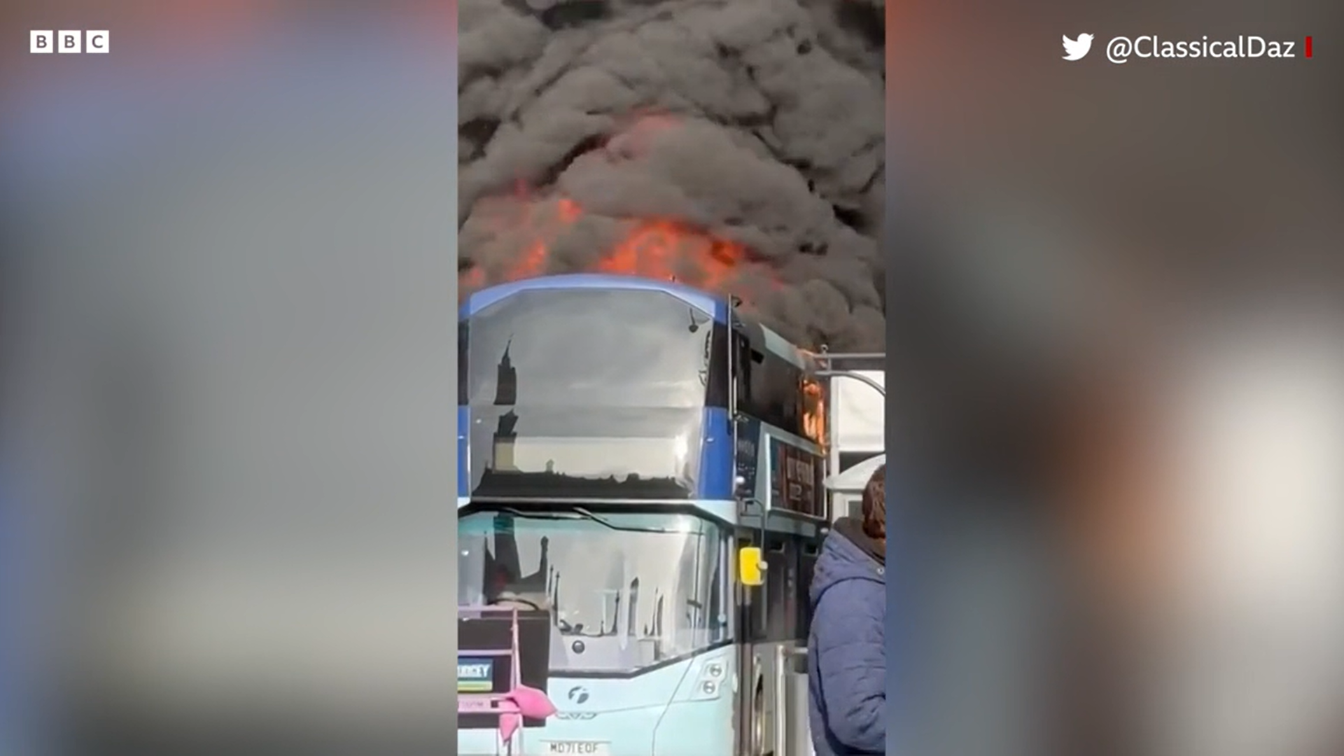 Mobile phone footage of a bus on fire with black smoke billowing from it