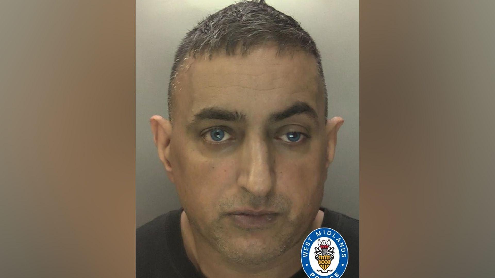 Police mugshot of a man with short dark hair, wearing a black T-shirt. The background is plain grey and there is a West Midlands Police logo imprinted on the picture.