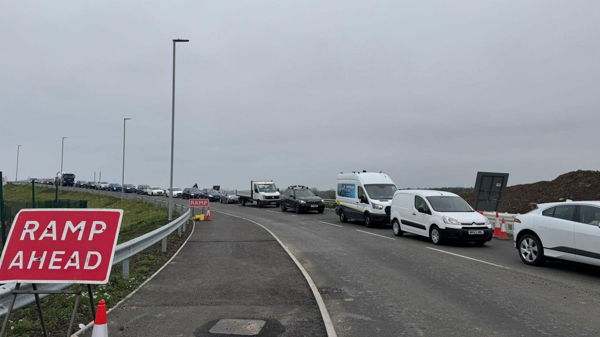 A long row of traffic builds up beyond a 'ramp ahead' sign.