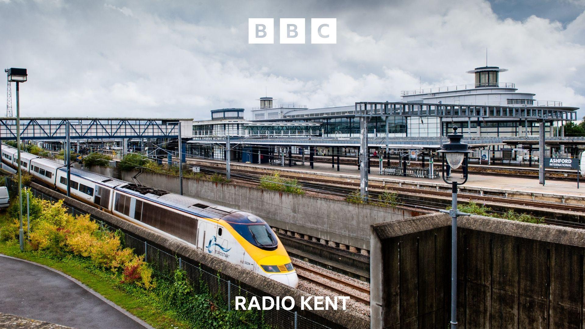 A Eurostar train passes Ashford International station, empty platforms can be seen in the middle distance.