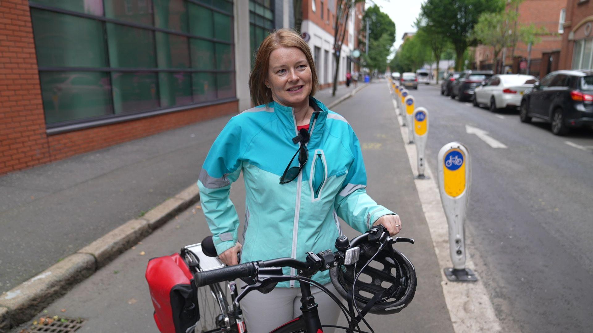 Anne Madden from the charity Sustrans. Anne is standing holding a bike and is wearing a blue coat.