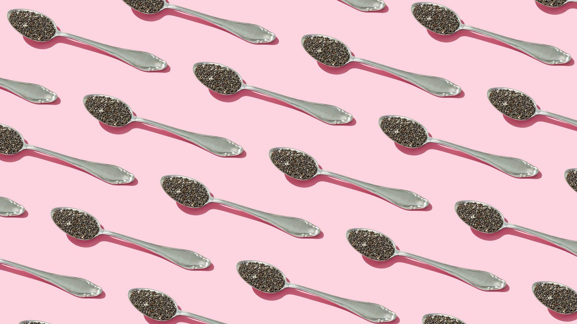 Diagonal silver teaspoons with chia seeds on them on a pink background.