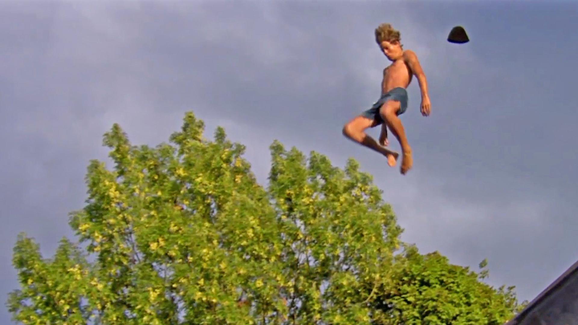 A man flies through the air as his hat blows of his head