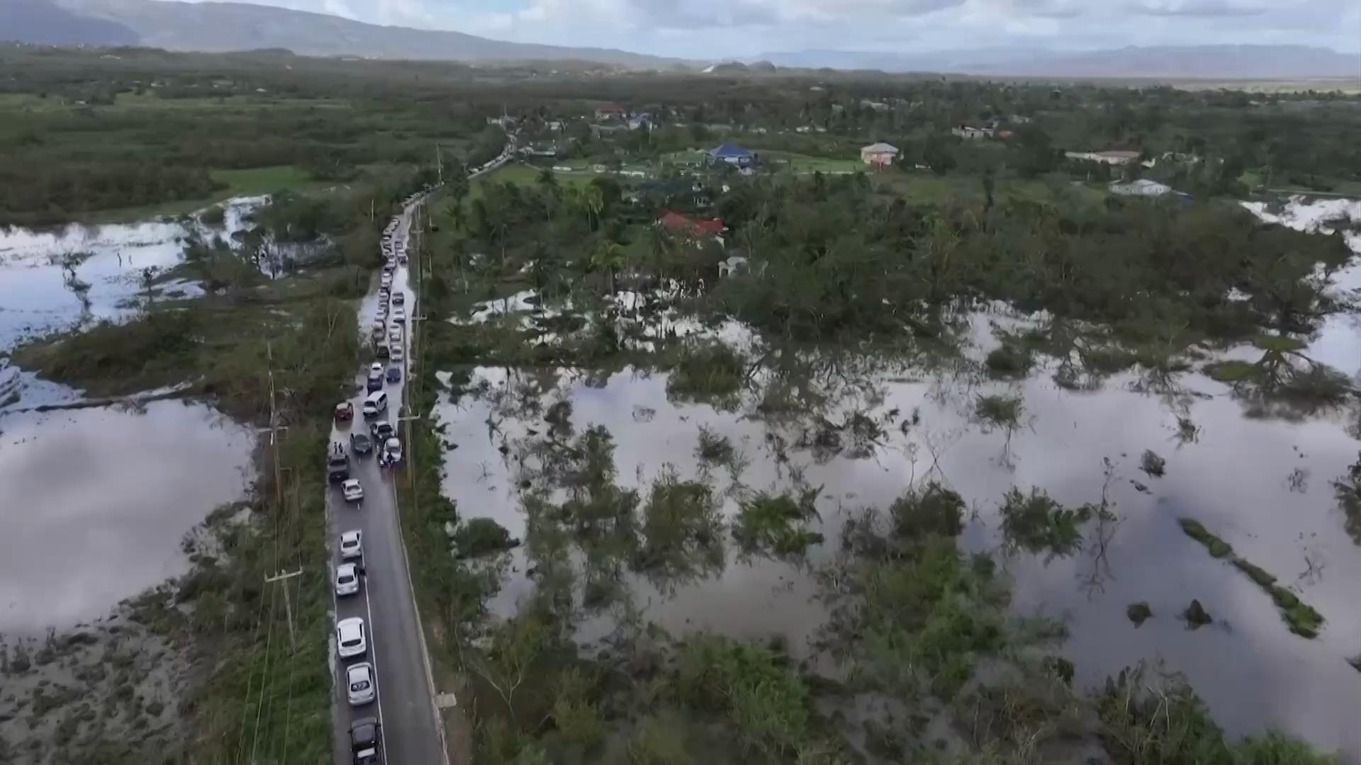 Cars are seen along a road which is surrounded by floodwaters