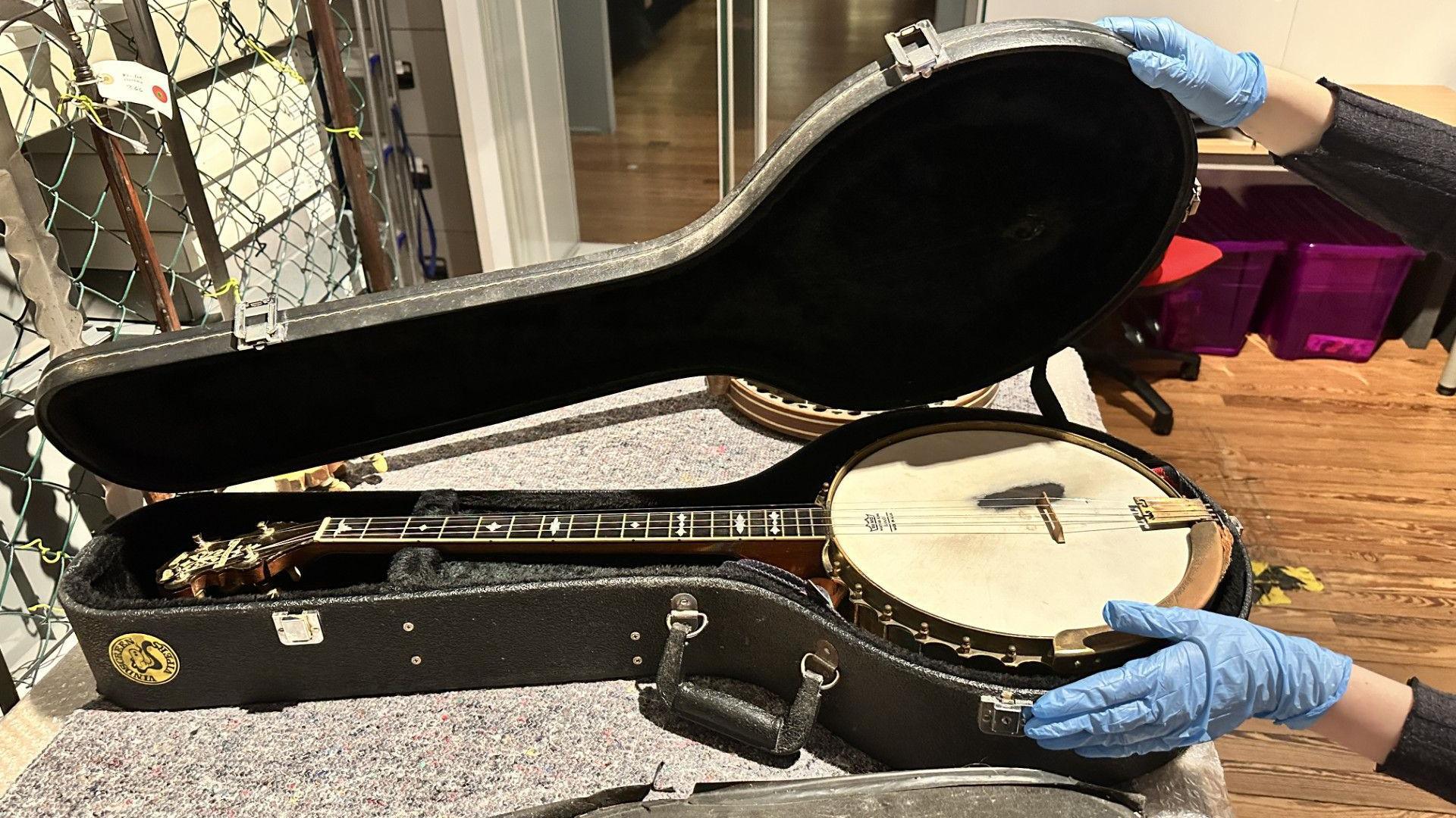 A banjo in a box. A hand in a blue latex glove is coming in from the left of shot to touch it.