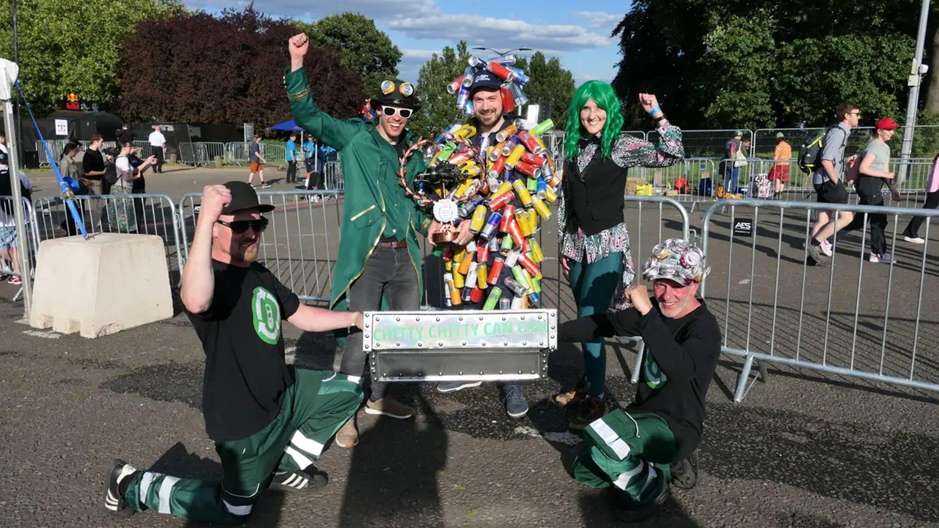 A team of five racers cheer, with one dressed in a suit made entirely of aluminium drinks cans