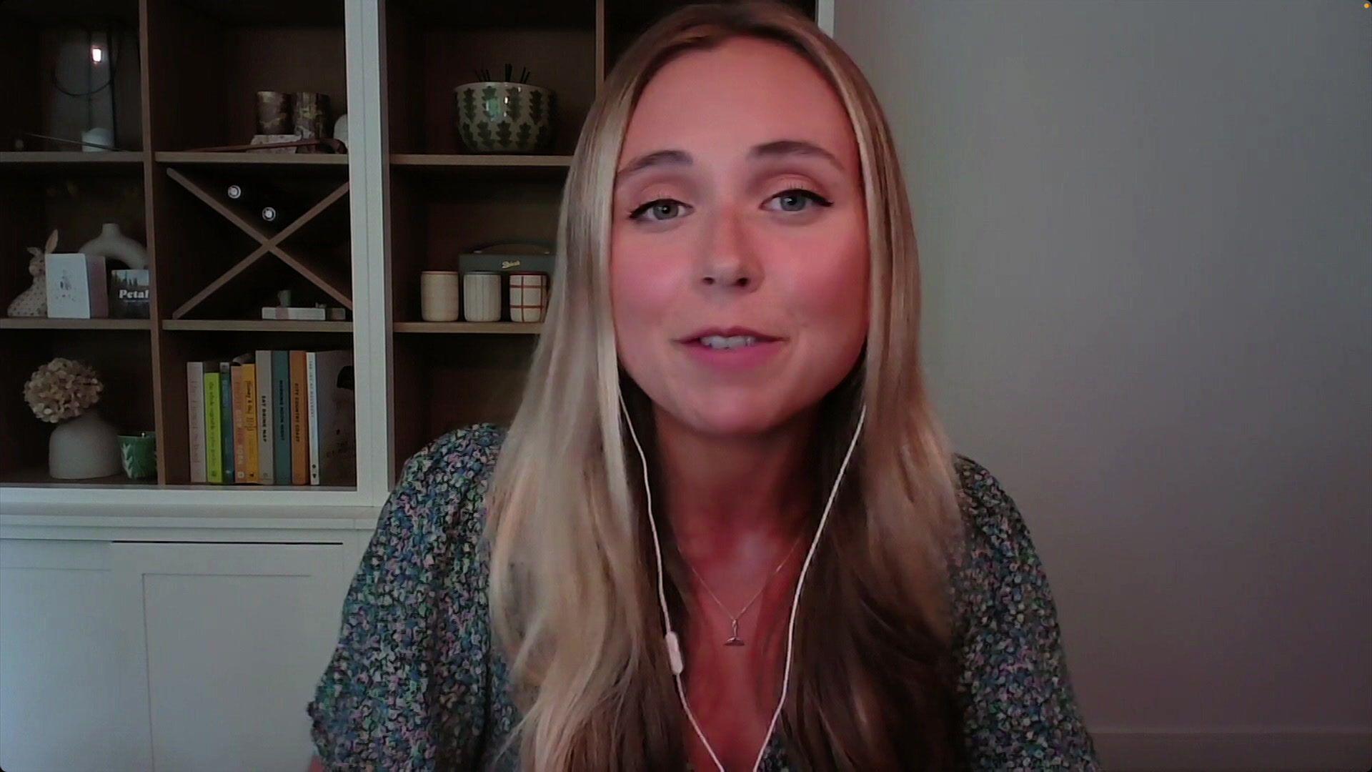 A woman with long blonde hair being interviewed. She is wearing a patterned top and headphones and looking into the camera.