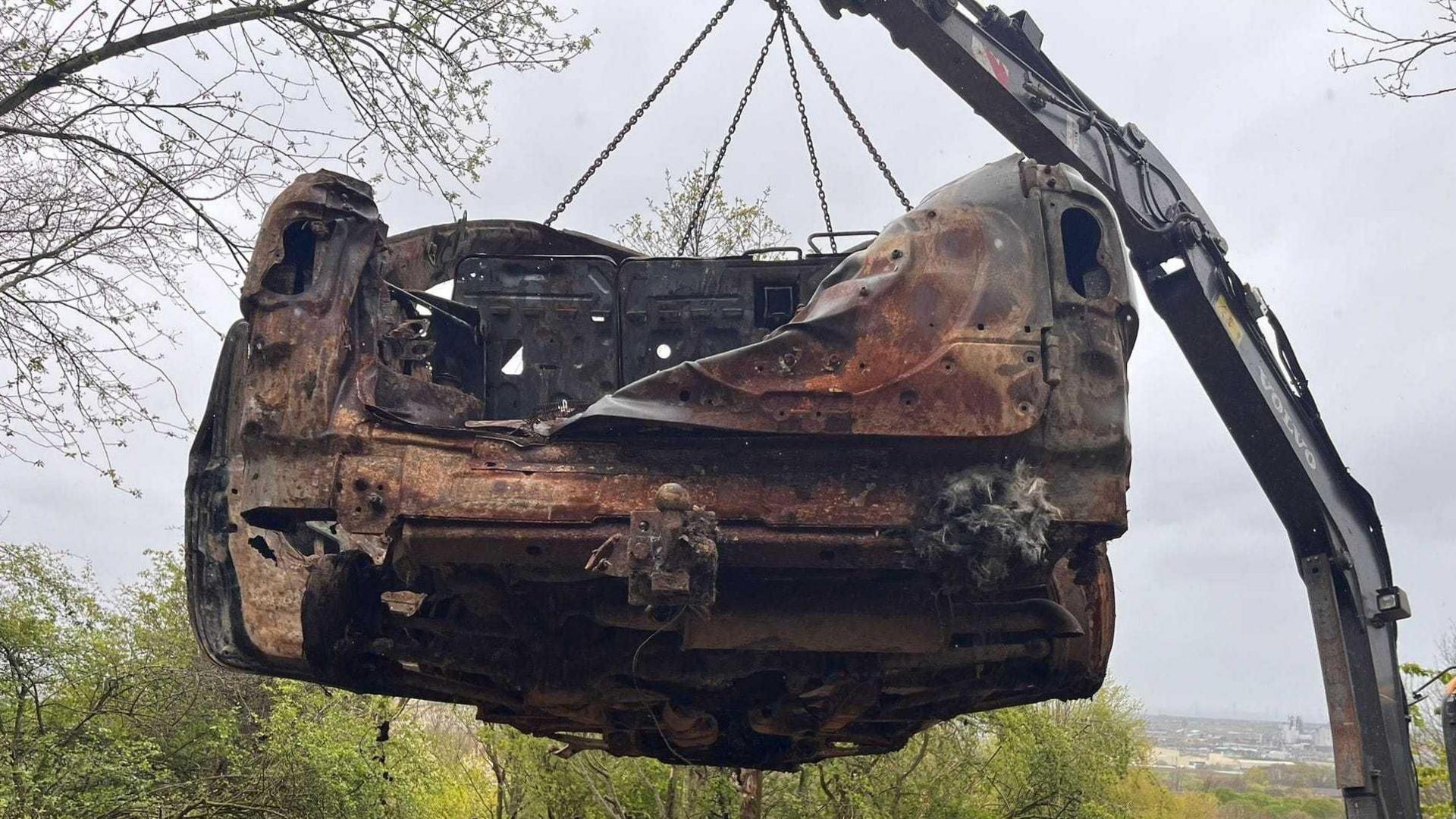 A crane lifts the burnt-out wreckage of a car from a beauty spot