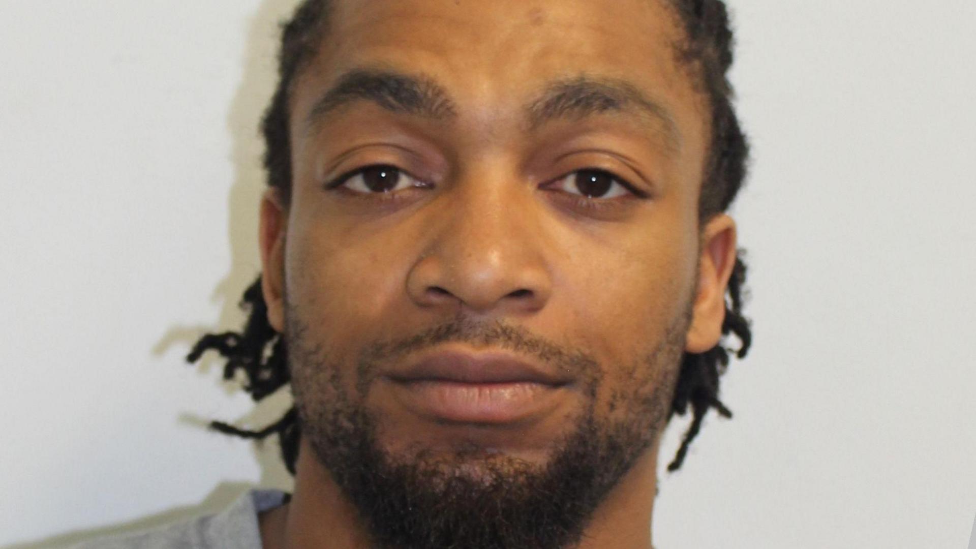 A Met Police custody image of Omar Wilson, a man with braided dark hair wearing grey t-shirt