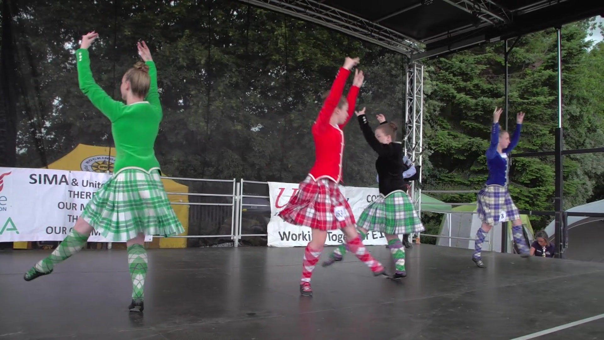 Four women wearing coloured tops and skirts dancing on a stage