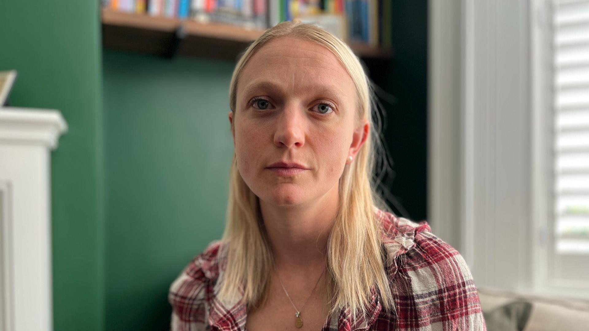 A woman with blonde hair and a red checkered shirt. She looks melancholic. 