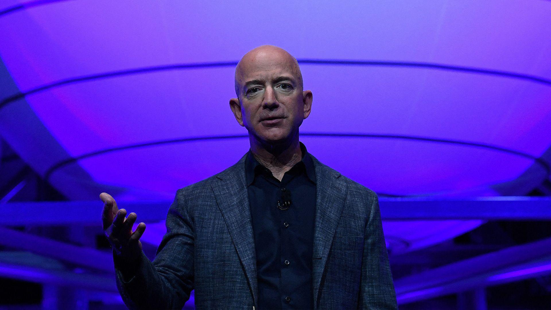 Amazon owner Jeff Bezos wears a blazer and holds his hand out at a conference.