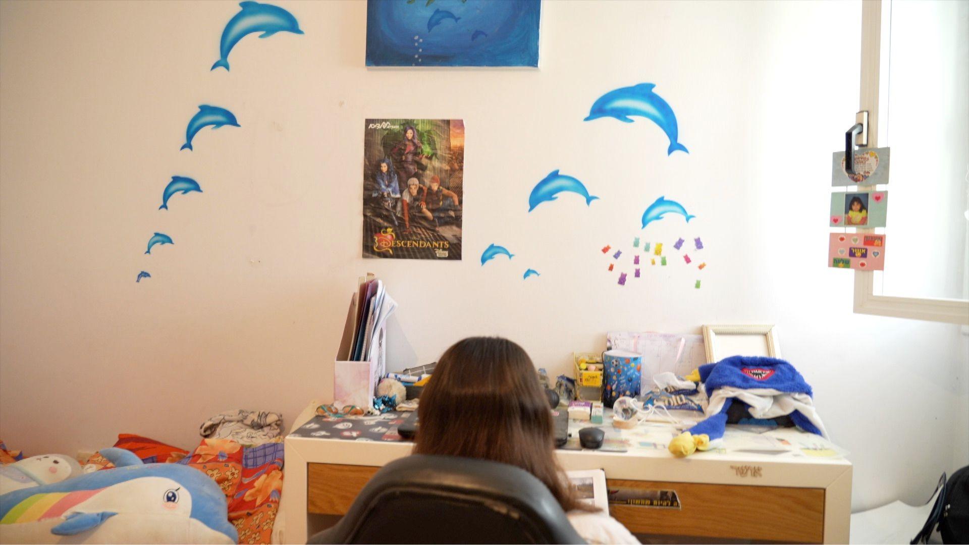 Back view of Osher sitting at a desk, with dolphins on the wall in front of her