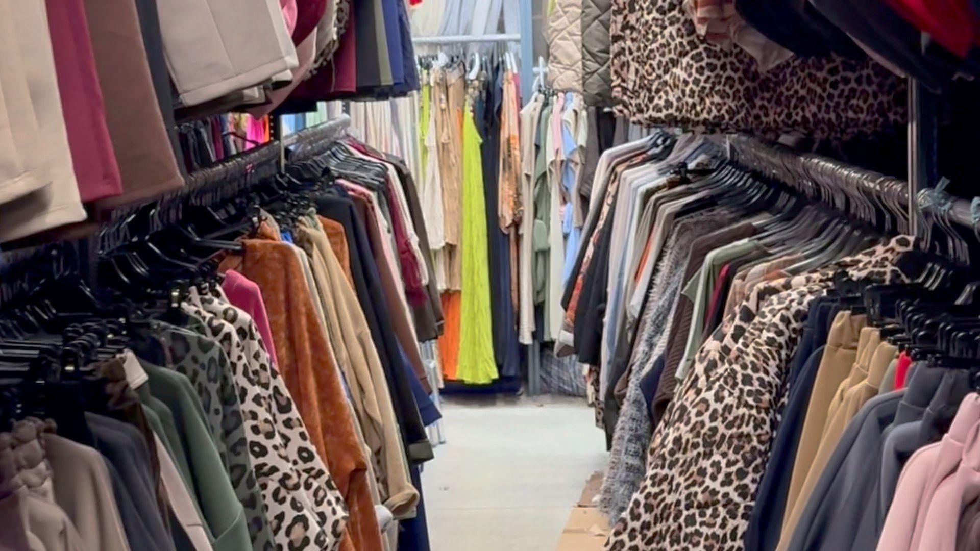 Looking down the middle of an aisle of clothes in a warehouse.