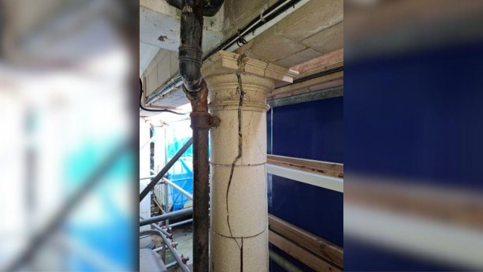 A large cream concrete column on what appears to be a building site. The column has a large crack running from top to bottom