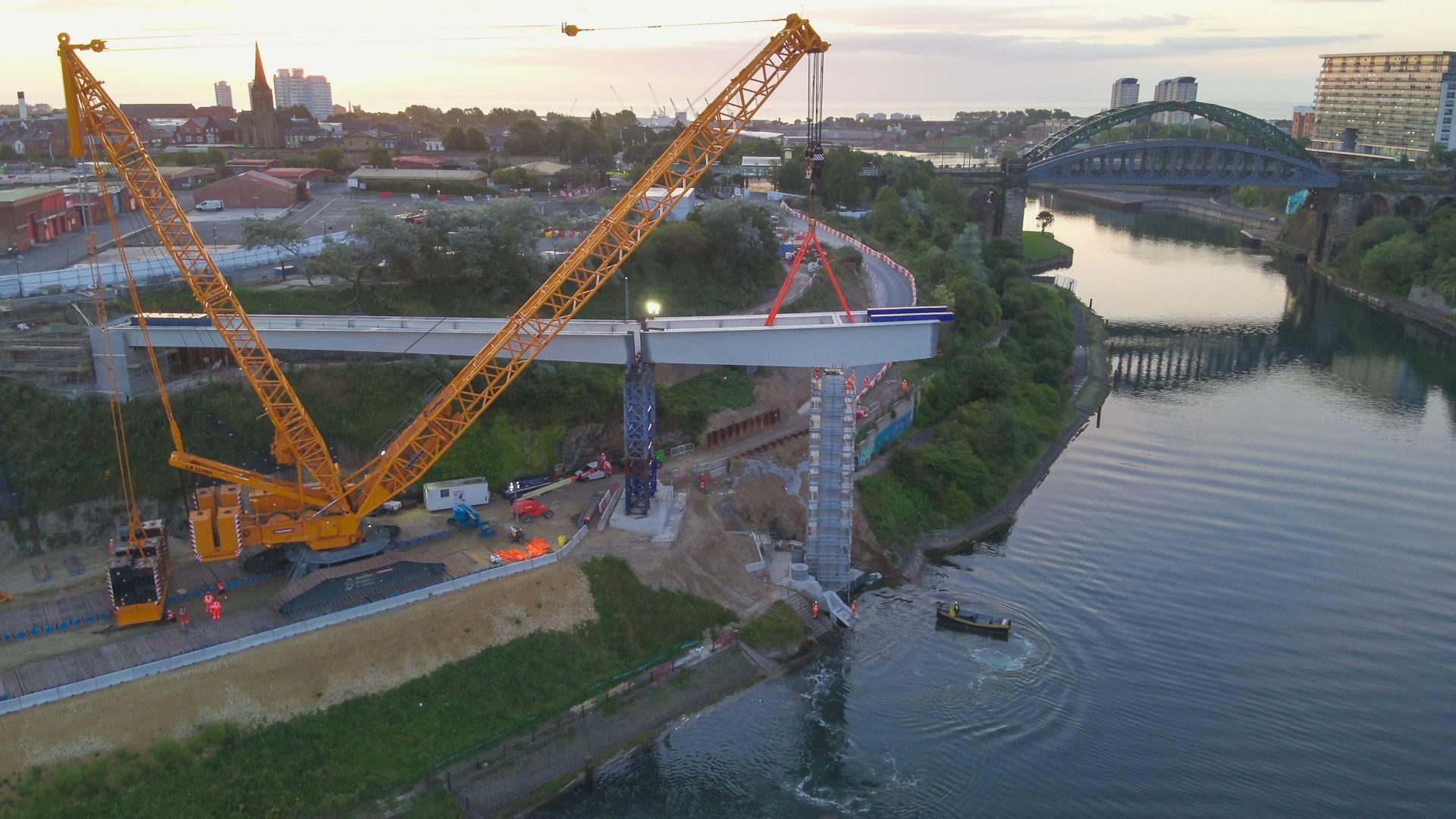 A yellow crane holding up a section of the steel frame. The river is to the right of the photo.