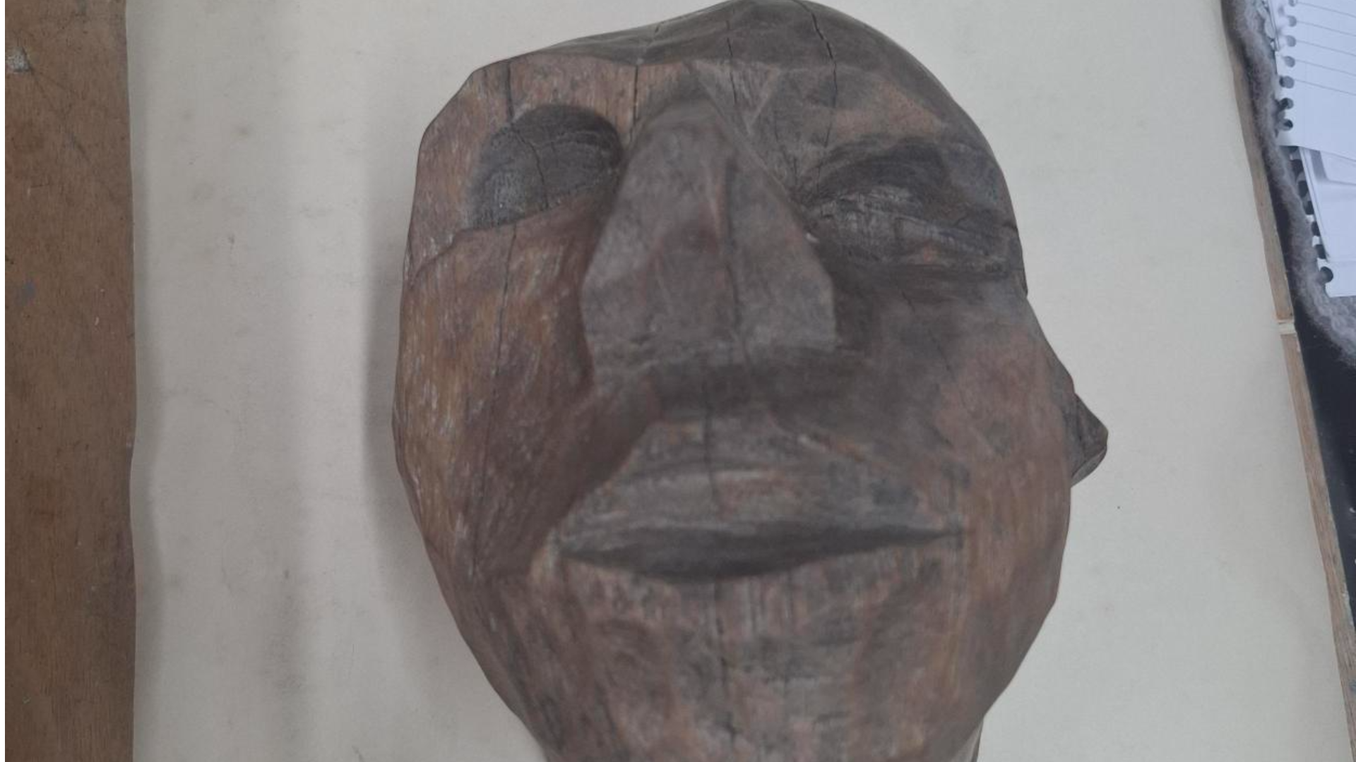 A wooden sculpture of a man's face on a white board.