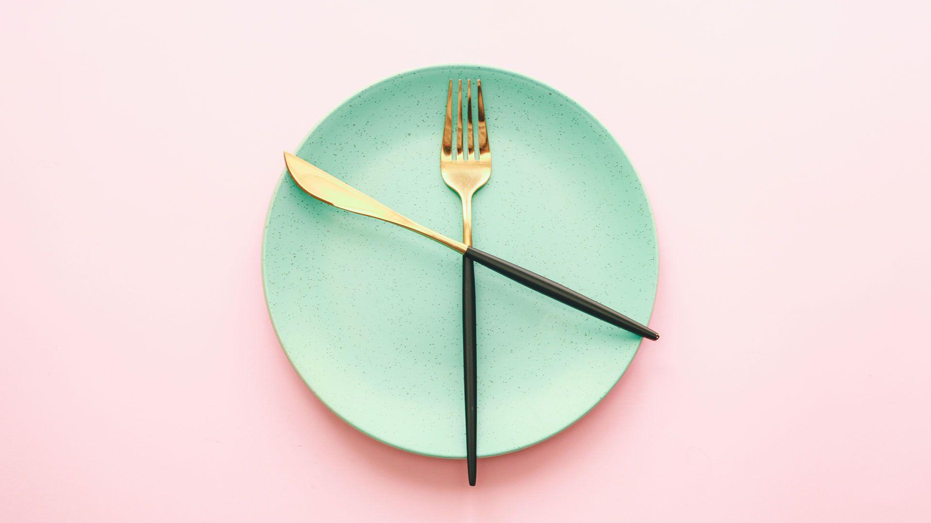 An empty plate with knife and fork across it, together it looks slightly like a clock.