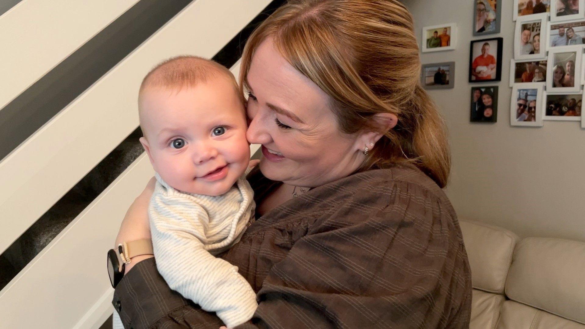 Rachel holds baby caleb close to her face and he is smiling while looking at the camera 