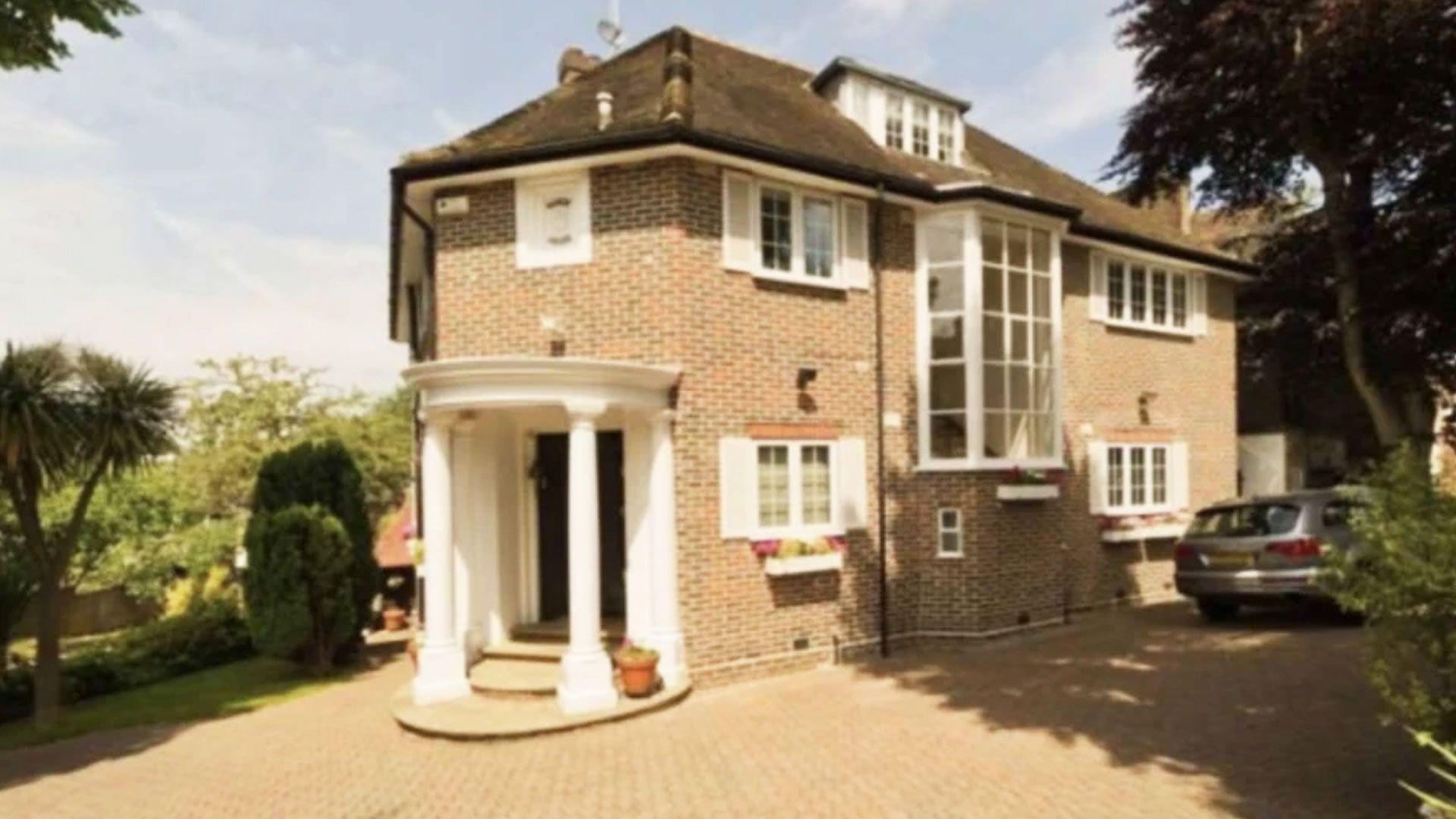 A large house in Hampstead - a white pillared portico, and red brick. A large tree is at the end of the driveway. 