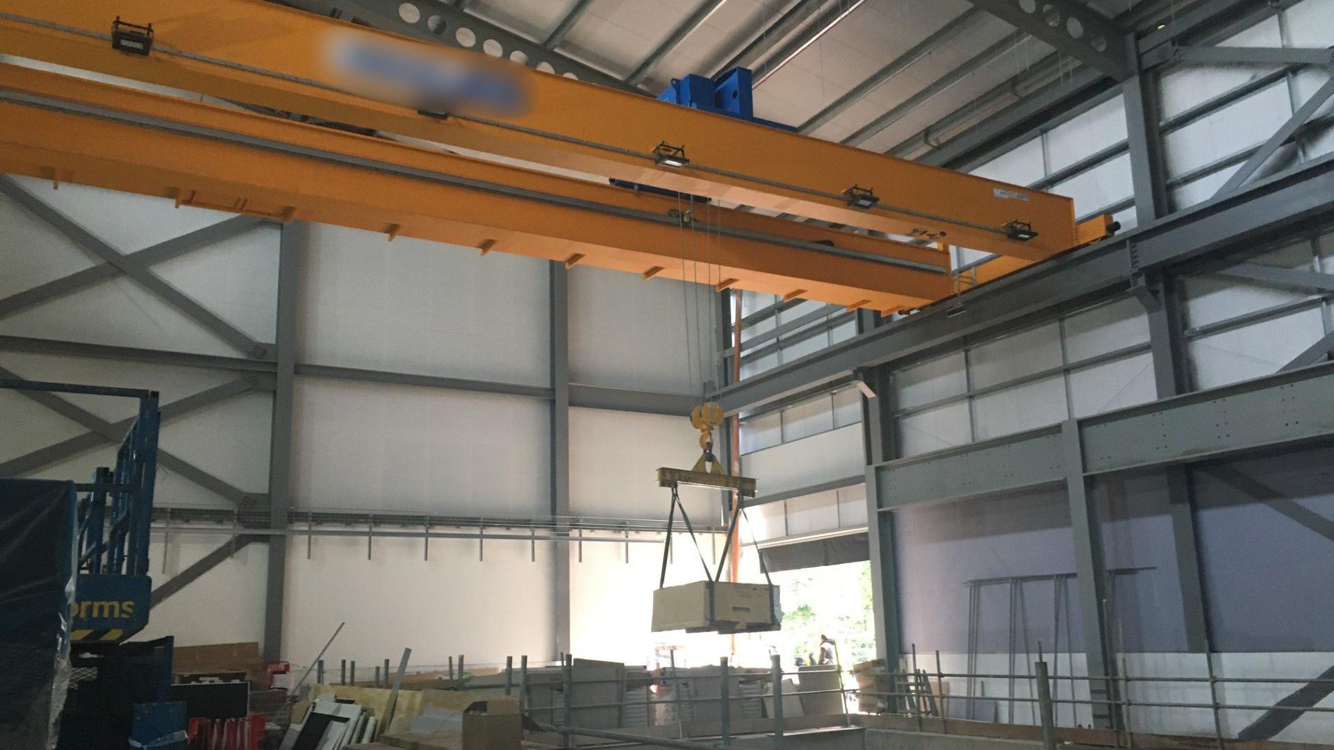 A huge crane in a half-built warehouse at the University of Birmingham. The crane is yellow and materials are hanging in the air. 