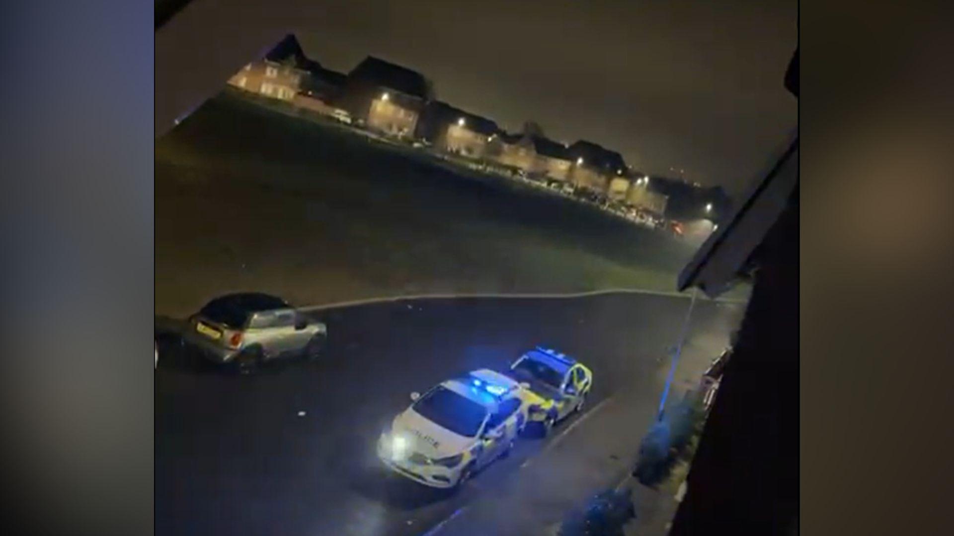 Police cars on blue lights with a crowd on the distance