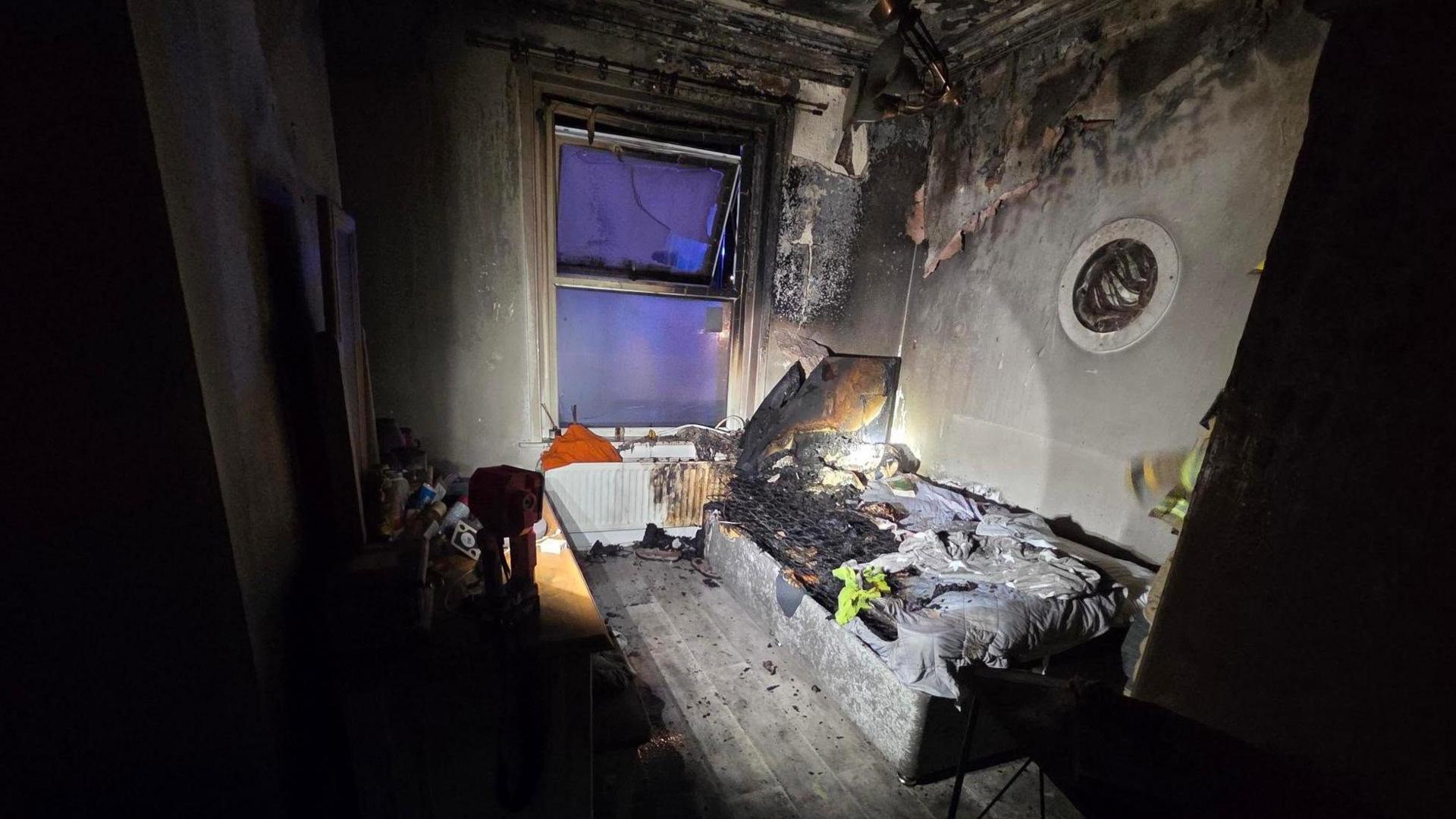 Bedroom with bed and dressing table and window at one end left charred after a fire