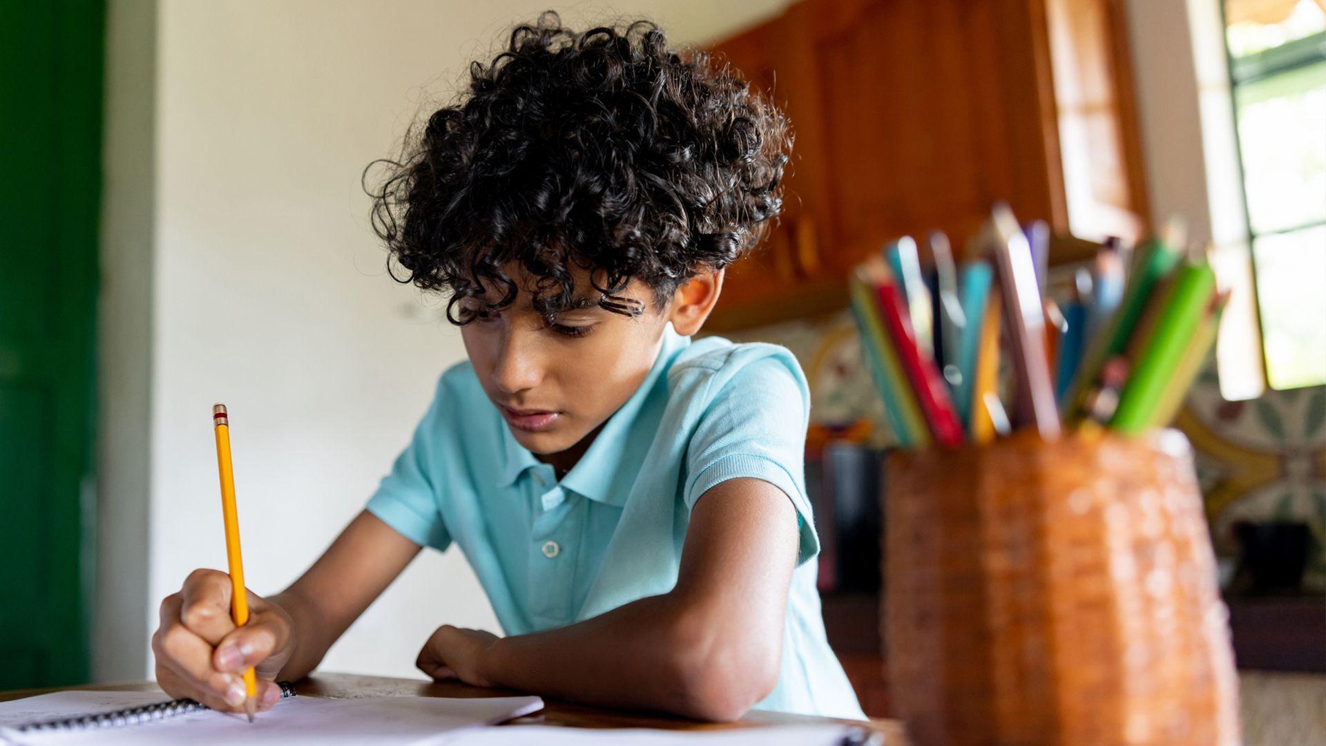 A young boy sits on a table at home writing 