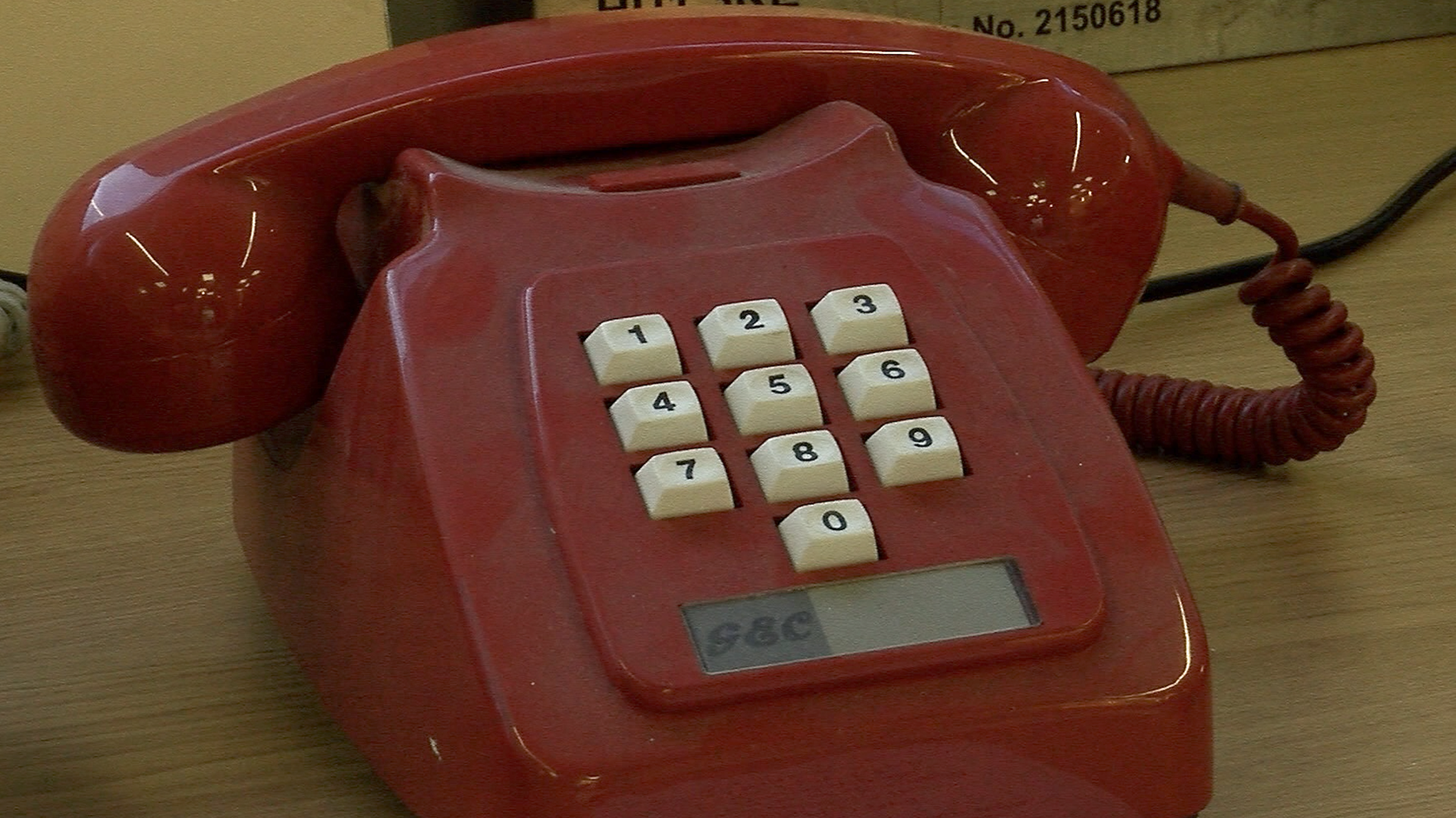 A mid 20th century push-button phone. It is dark red, with white buttons and a cradle for the handset.