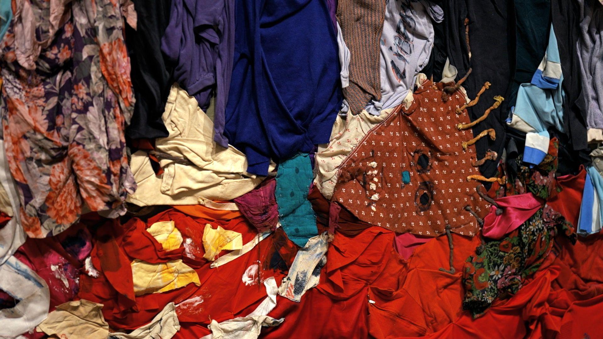 Colourful textiles and other found materials, forming an abstract scene of a figure lying on the ground.