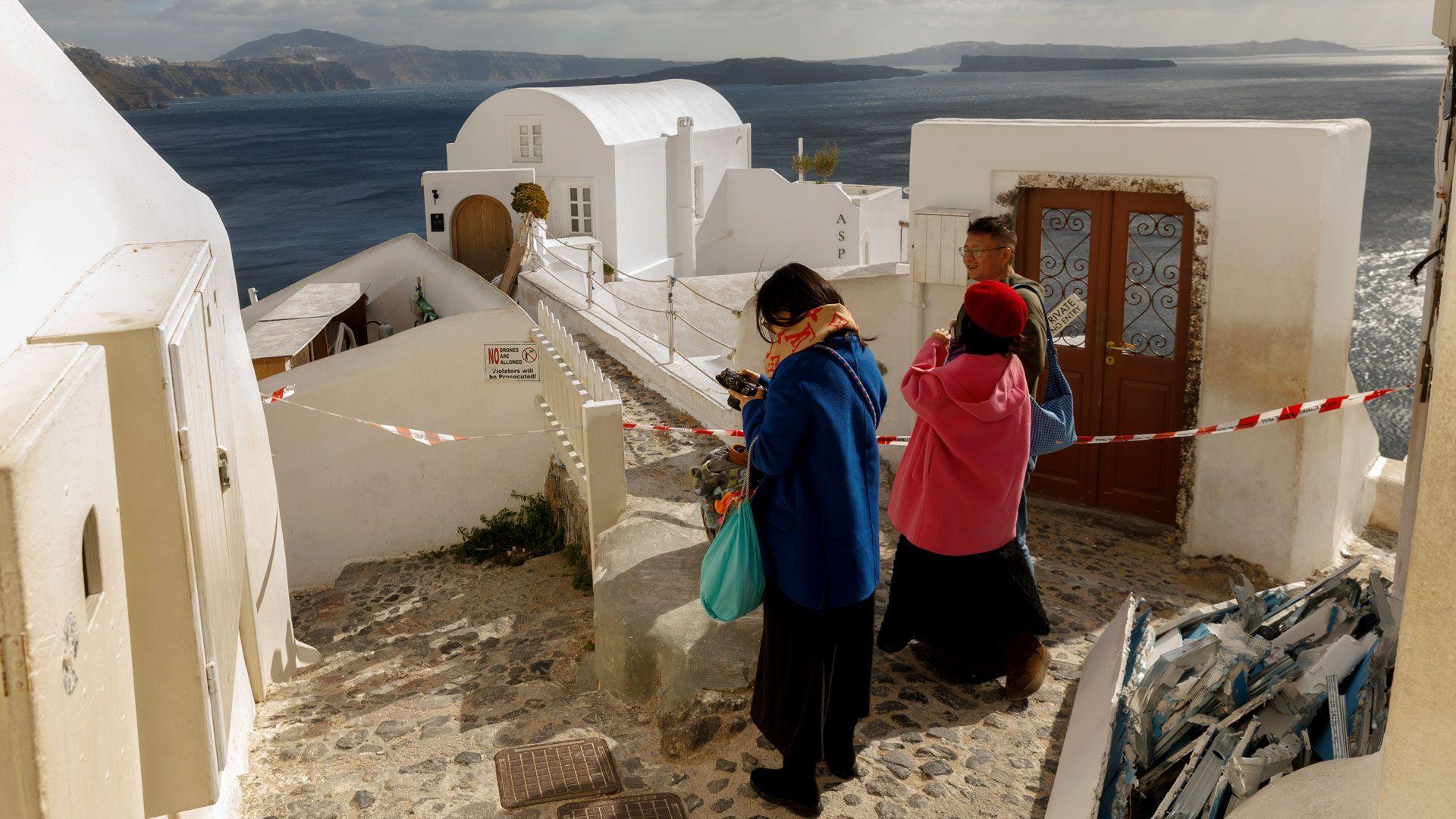 People stand beside taped off houses on a hill top overlooking the sea