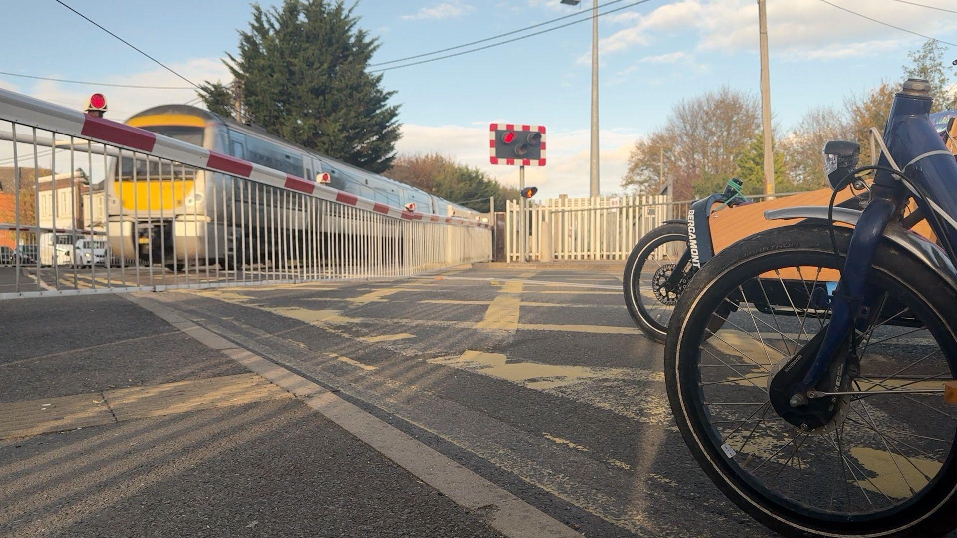 Two cyclists are waiting at a level crossing while a train passes.