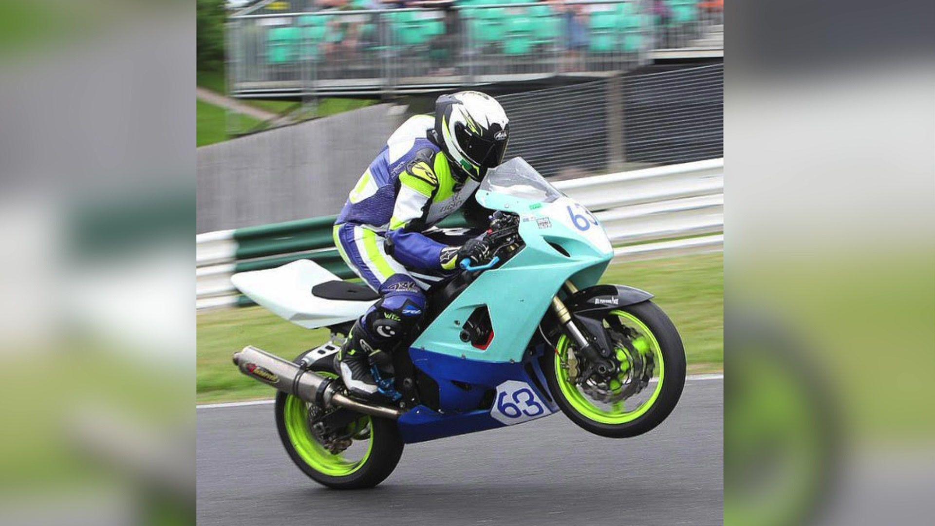 Robert Bush riding a motorbike on a race track. He is wearing blue white and green leathers and a white helmet and sits in a crouched position over the handlebars. The bike is coloured blue, green and white.