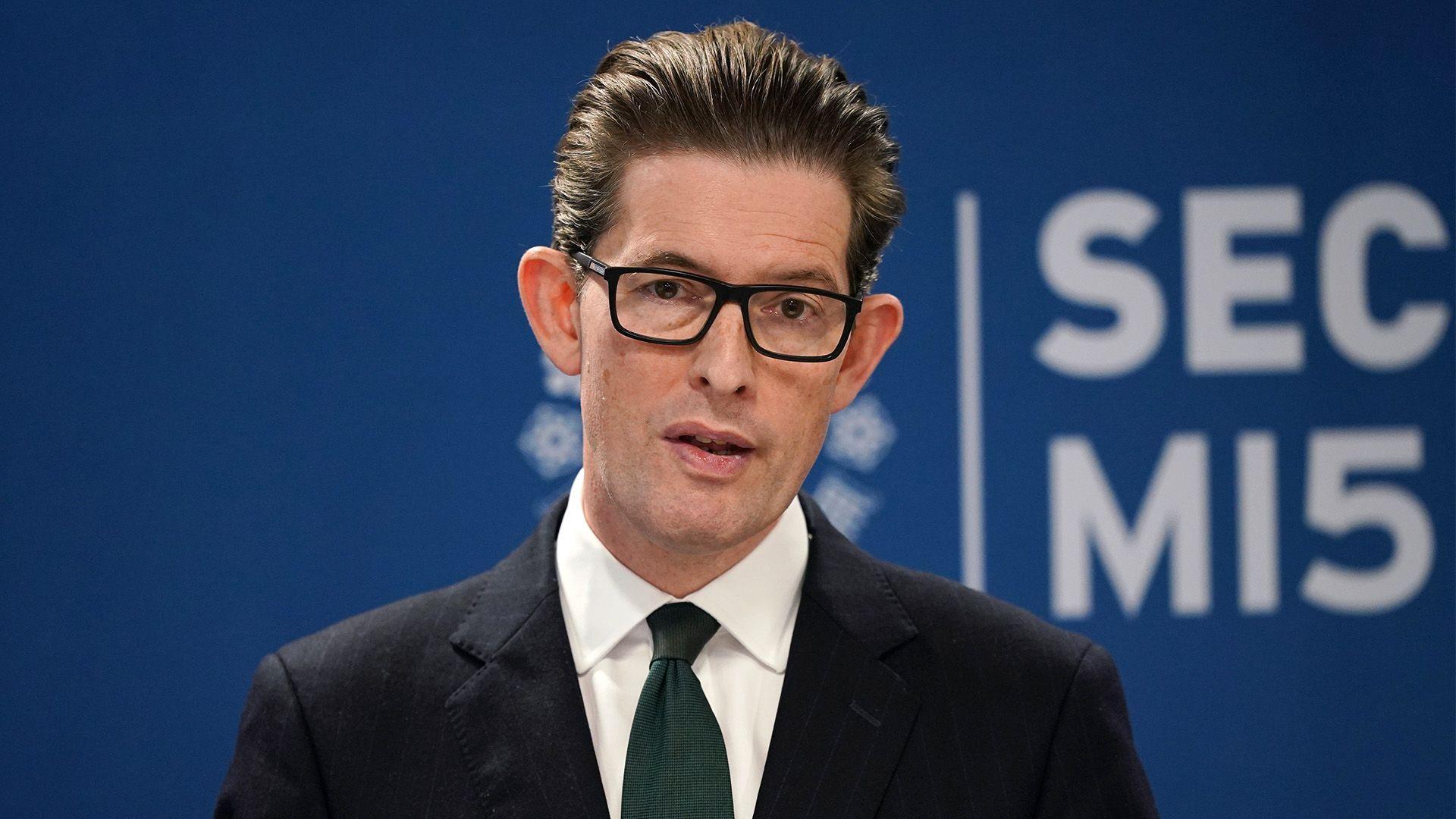 Ken McCallum, Director General of MI5 - a middle-aged man with slicked back dark brown hair, and wearing dark-rimmed rectangular glasses. He is wearing a dark suit, white shirt and navy blue tie.