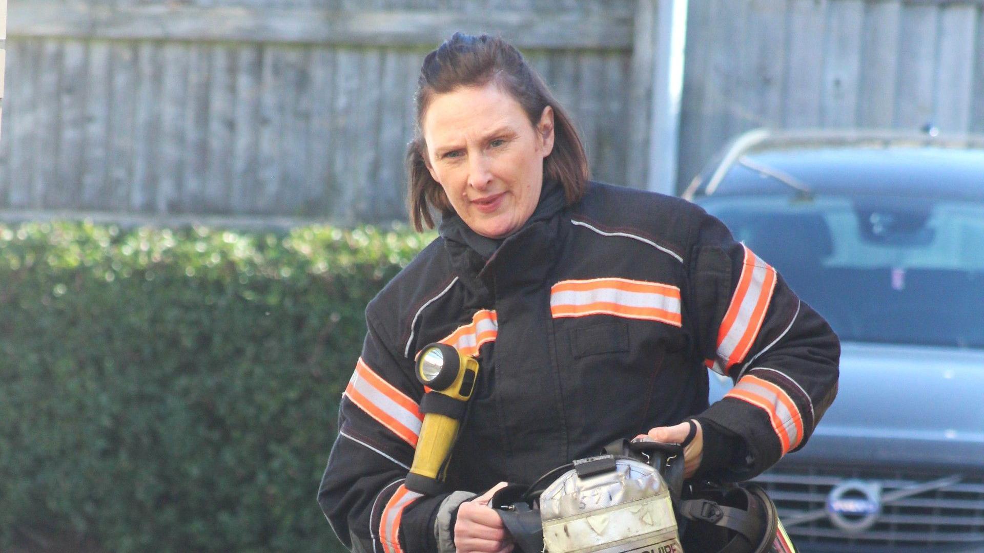 Ms Bourne is carrying a silver oxygen tank during a training exercise. She has a look of concentration as she walks.