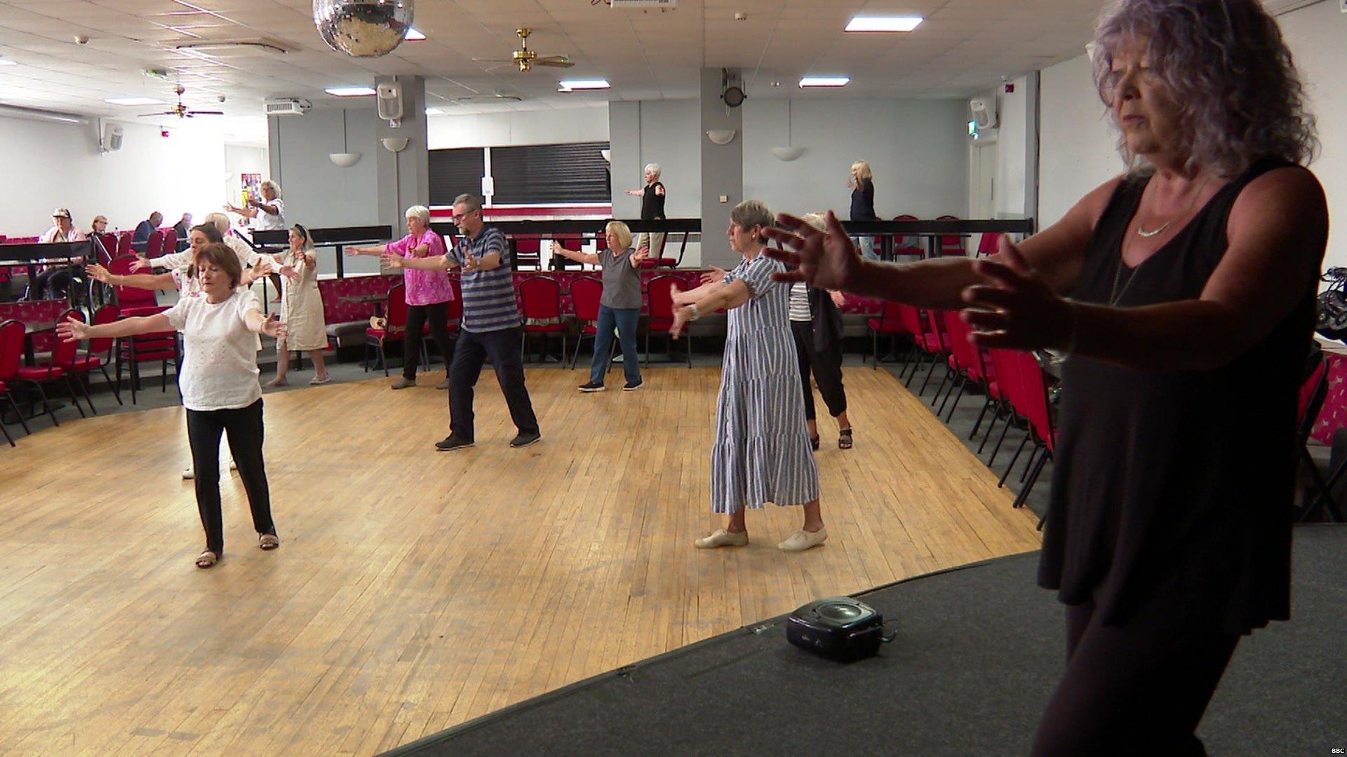 A group of people do Tai Chi class in a hall