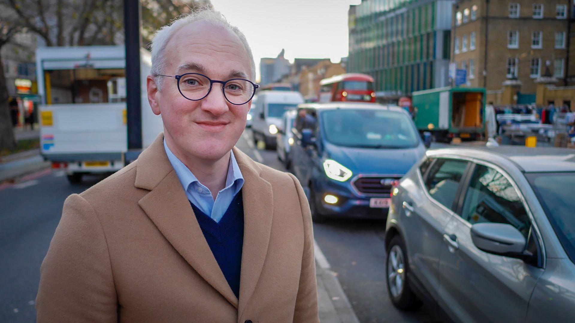 James Gallagher stands on a road busy with traffic.