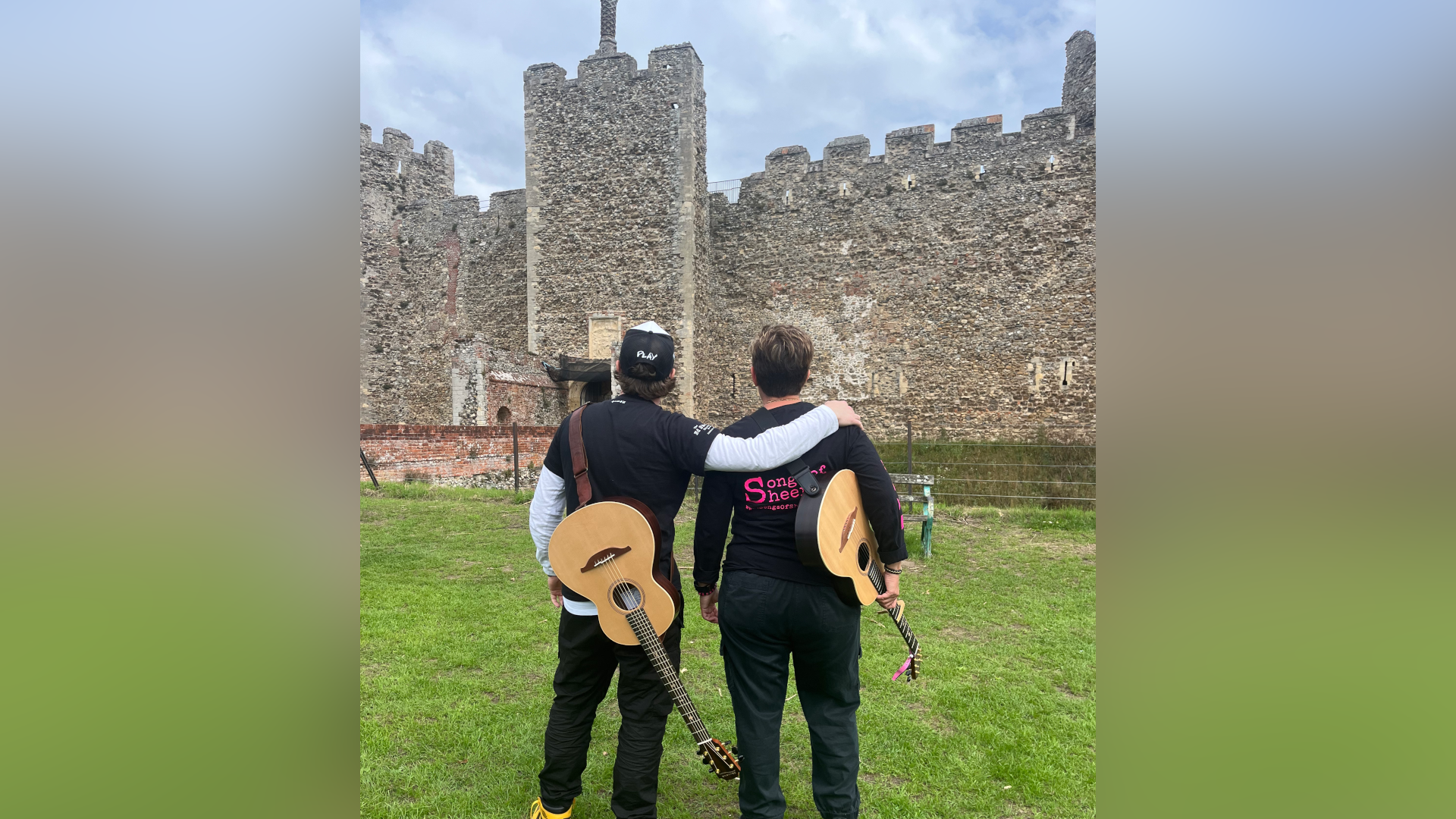 Mr Plamondon and Ms Judge face away from the camera looking at Framlingham Castle. Their guitars rest on the sides of their bodies. Mr Plamondon has his arm around Ms Judge's shoulders.
