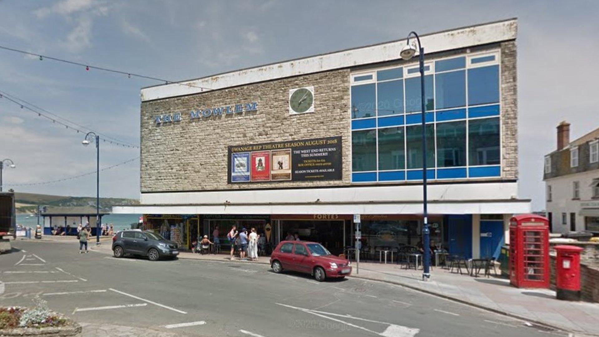 The front of the Mowlem Theatre in Swanage with cars passing in front and the sea in the background